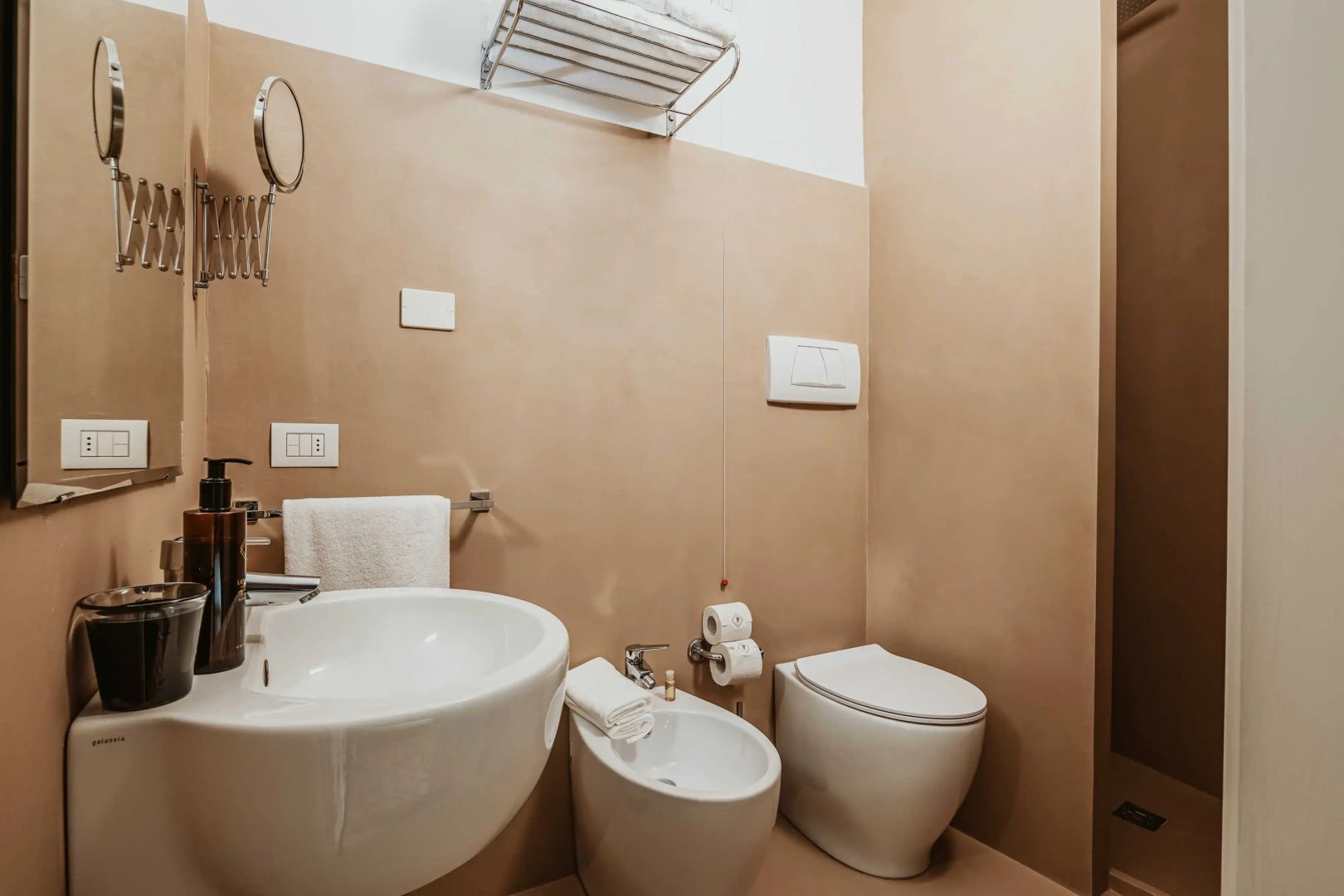 Modernes Badezimmer mit weißem Waschbecken, Bidet, Toilette und beigefarbenen Wänden.