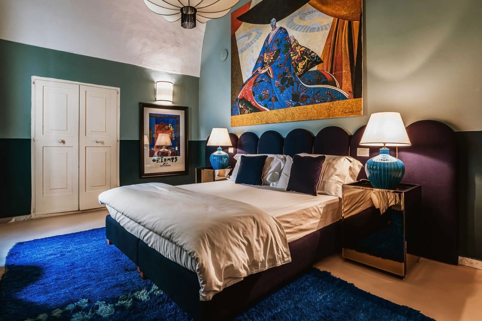 Schlafzimmer mit blauem Polsterbett, blauem Teppich und einem großen Gemälde an der Wand.