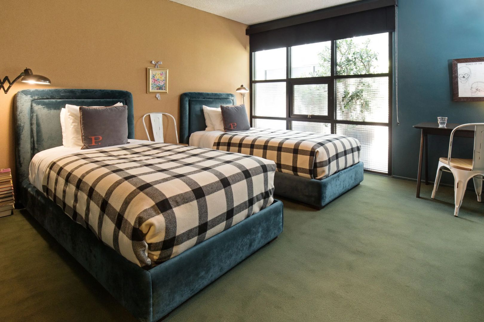 Hotelzimmer mit zwei Einzelbetten, karierten Tagesdecken und großen Fenstern vor gelber Wand.