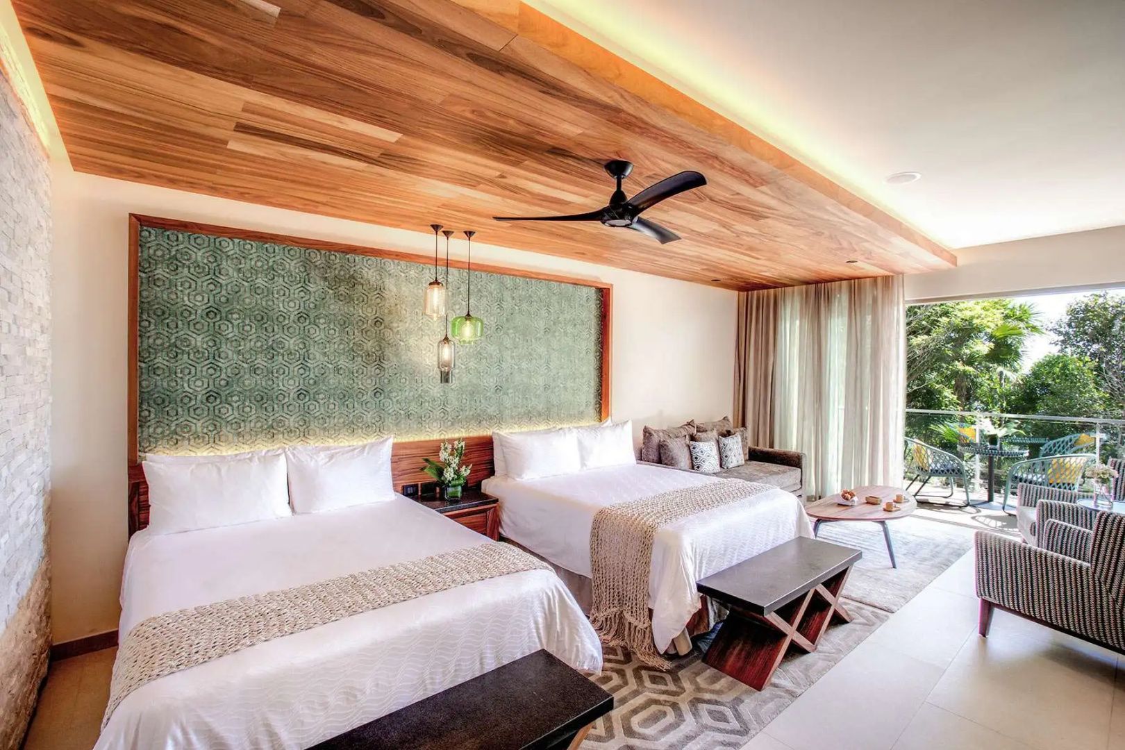 Ein helles Zimmer mit zwei Betten, Holzdecke, Deckenventilator und grünem Wandmuster.