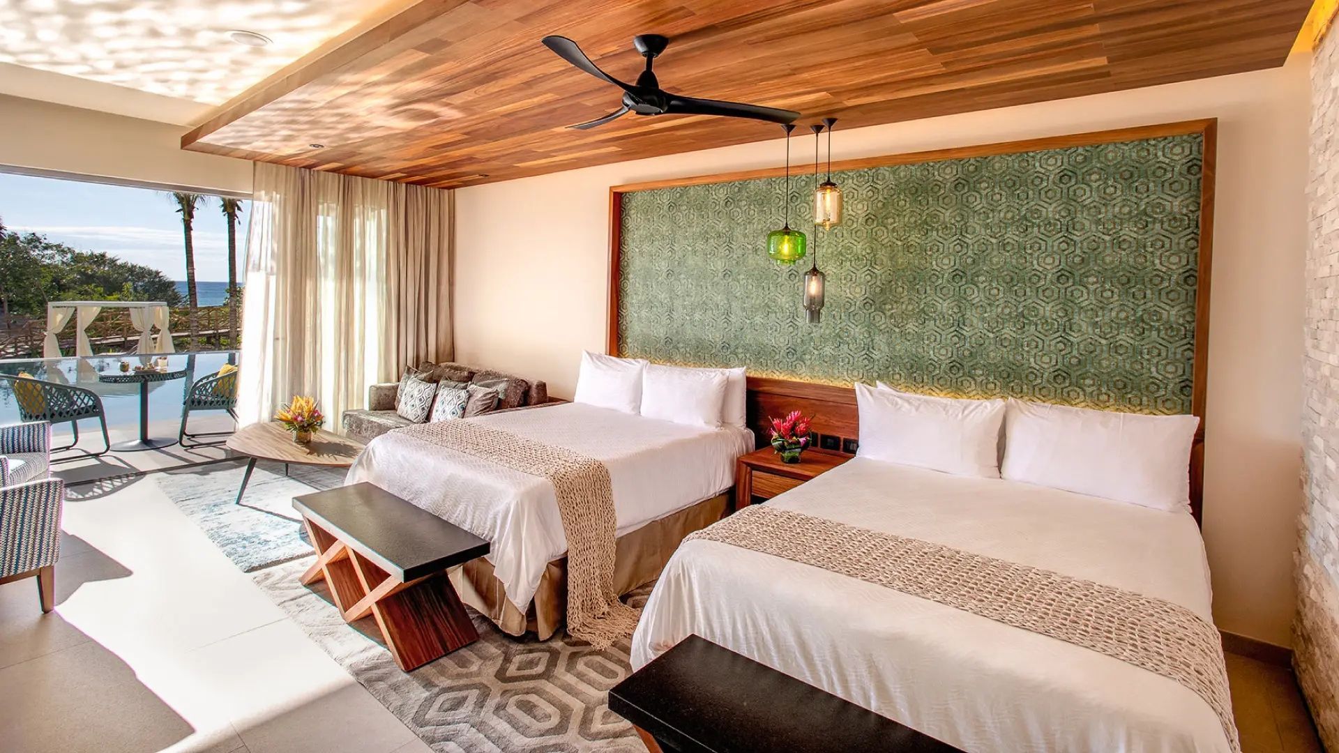 Hotelzimmer mit zwei Doppelbetten, Holzdecke, Deckenventilator und grüner Wandgestaltung.