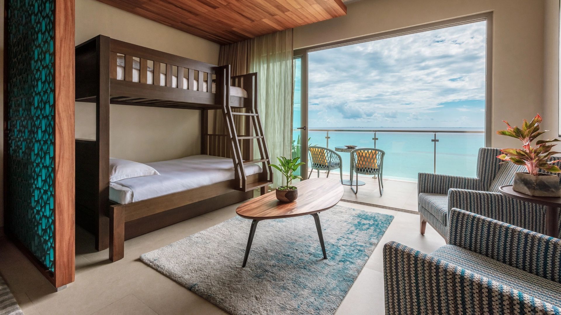 Hotelzimmer mit hölzernem Etagenbett, Couchtisch, Teppich und Balkon mit Meeresblick.
