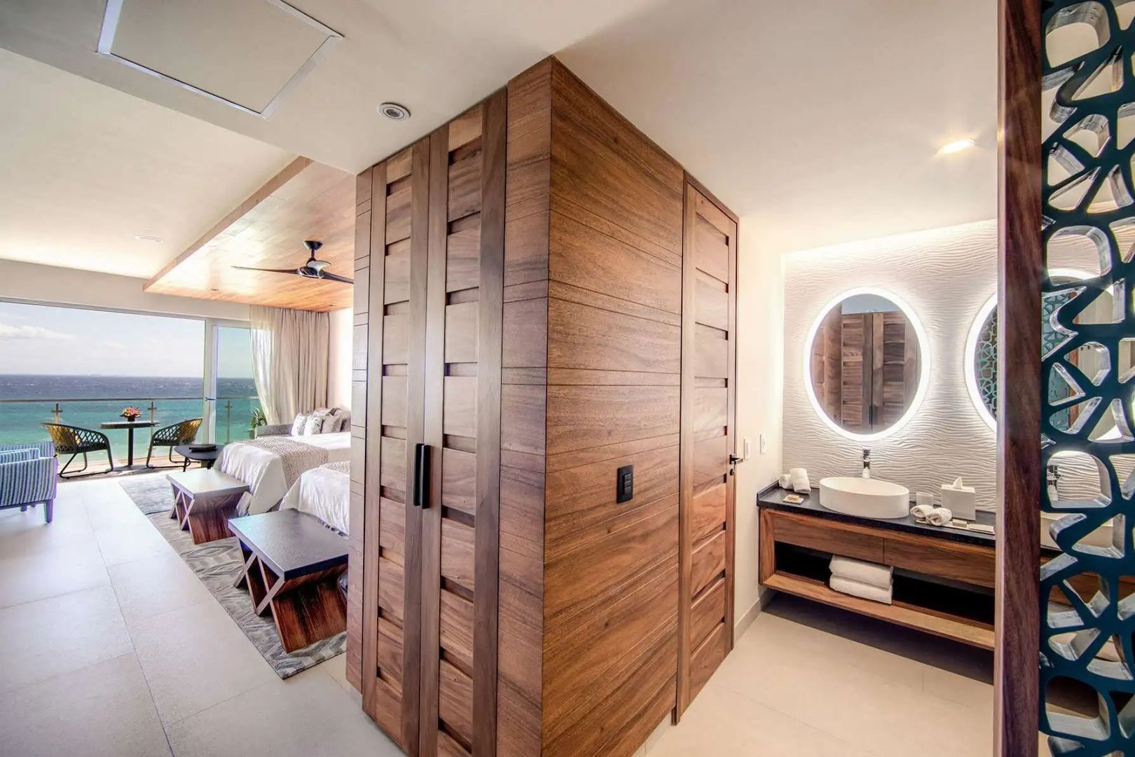 Eingangsbereich einer Suite mit Holzeinbauschrank und beleuchtetem rundem Spiegel.