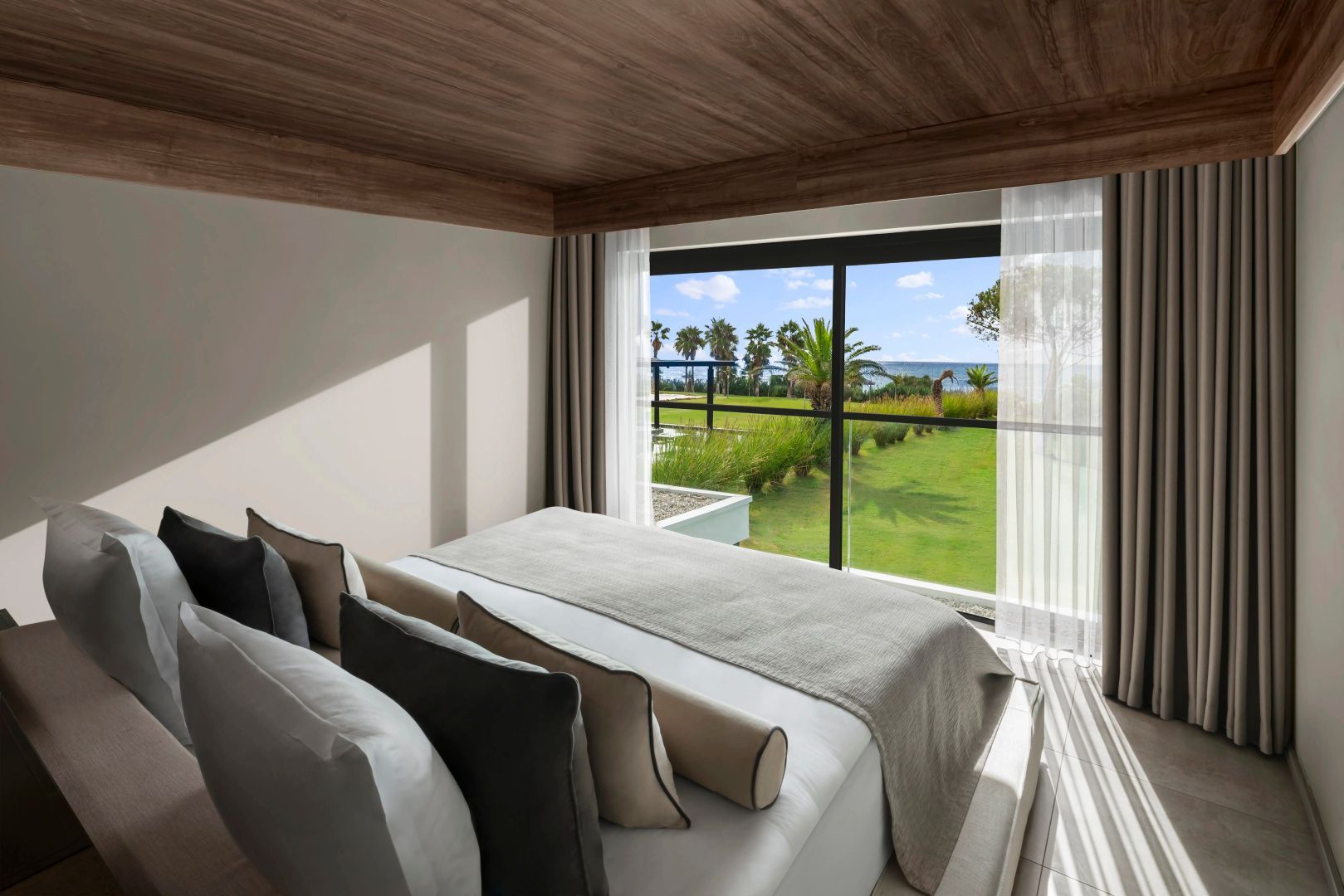 Doppelbett im modern eingerichteten Hotelzimmer mit Blick durch das Fenster auf den Garten und das Meer.