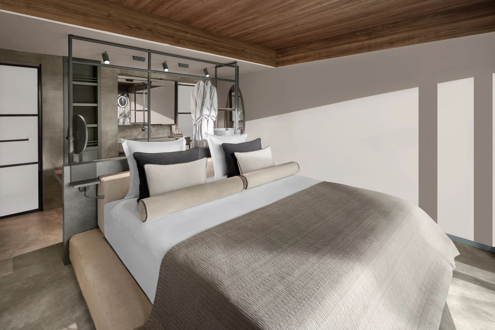 Doppelbett mit hellen und dunklen Kissen unter einer Holzdecke mit offenem Badezimmerbereich dahinter.