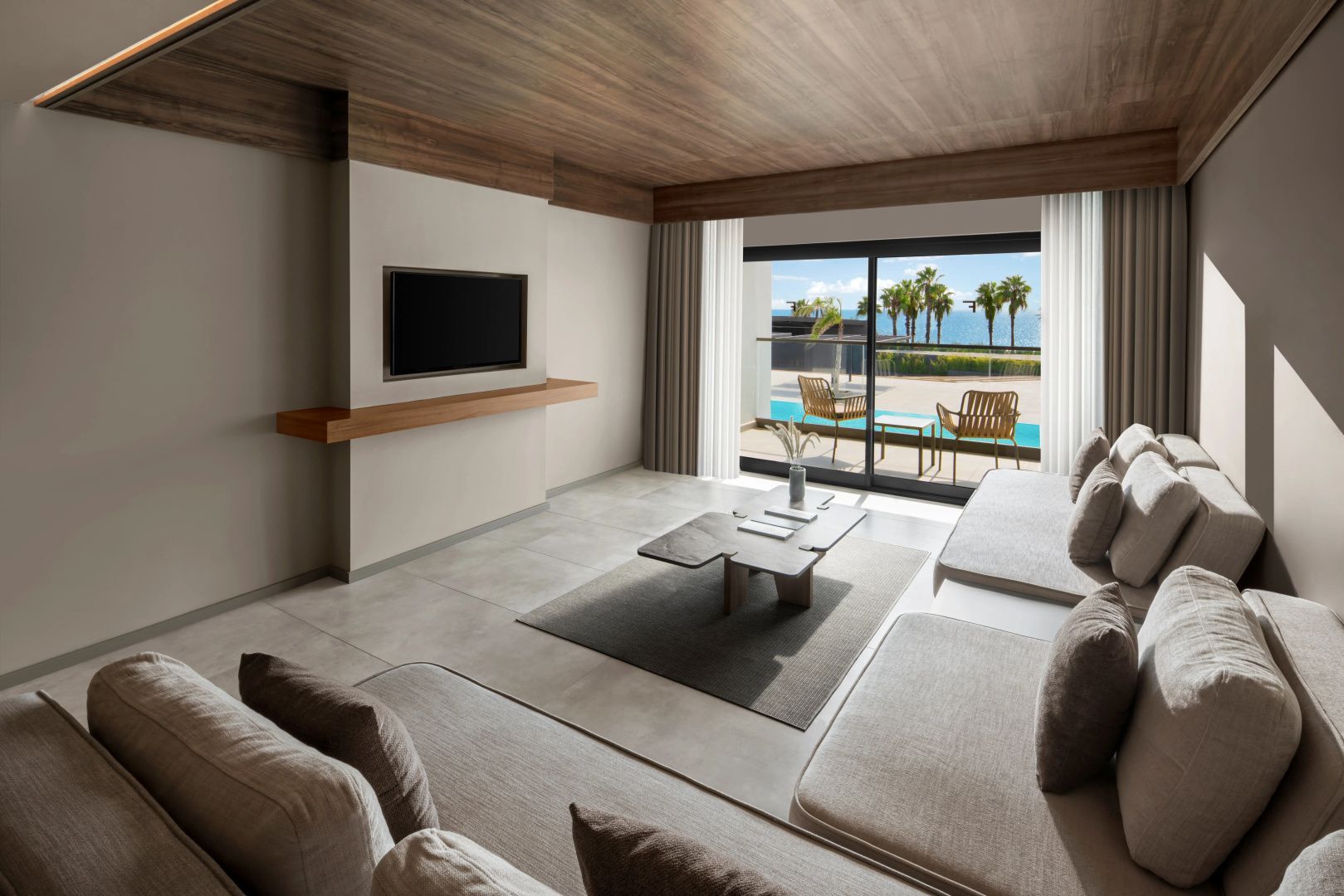 Modernes Wohnzimmer einer Hotelsuite mit Sofas, Fernseher und Blick auf die Terrasse mit Pool und Meer.