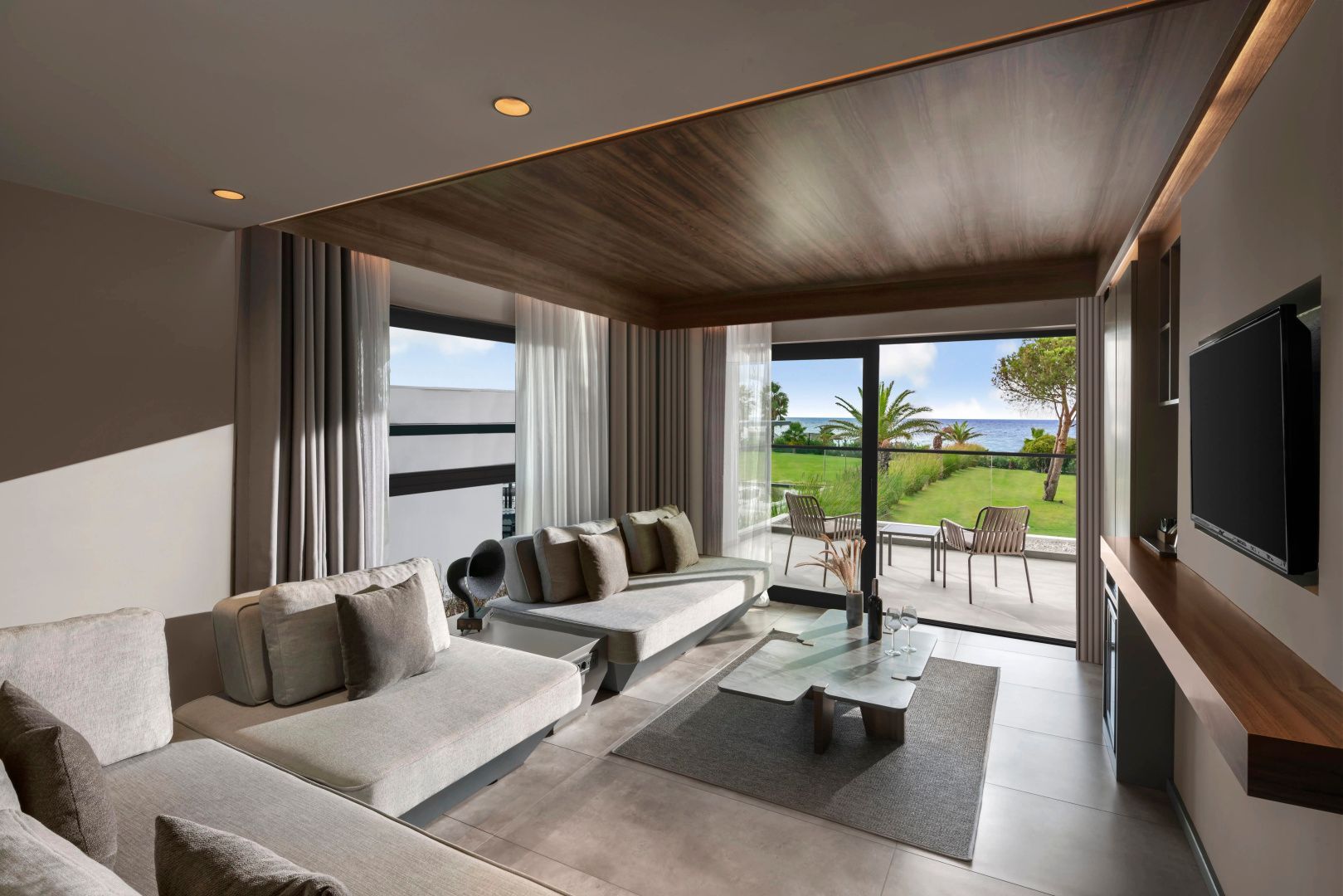 Moderner Wohnbereich mit hellem Sofasystem, Couchtisch und Zugang zur Terrasse mit Meerblick.