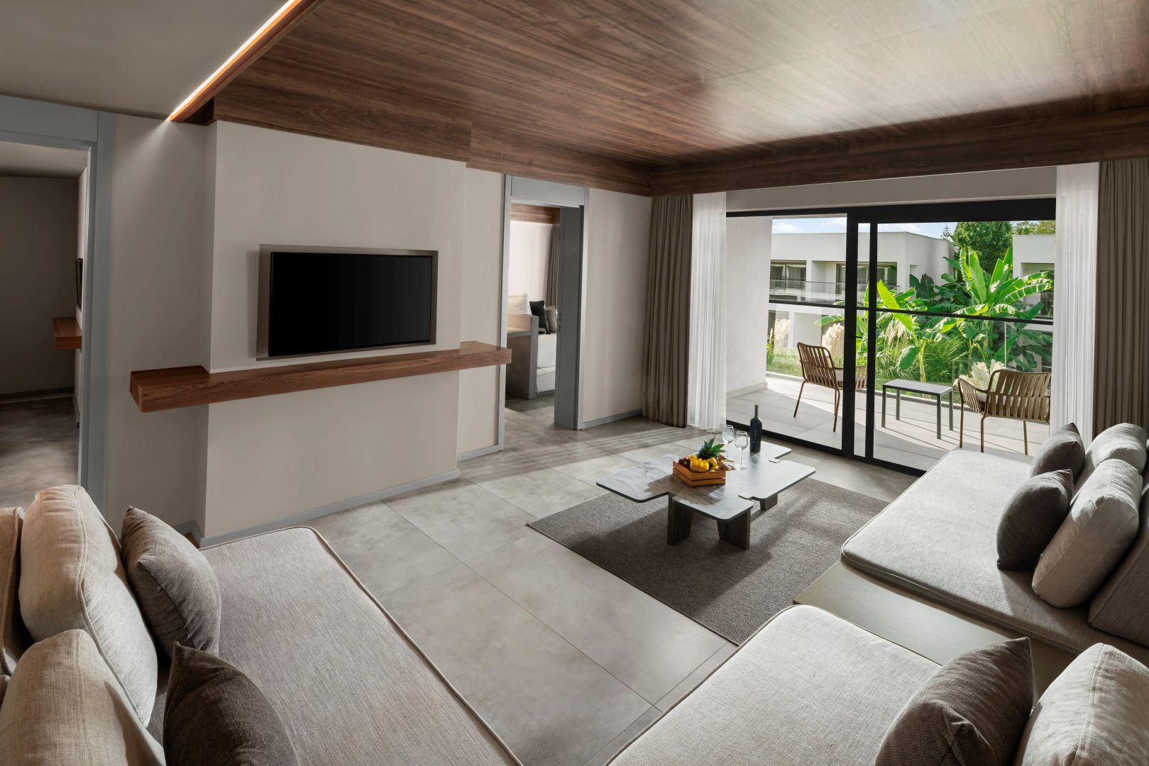 Wohnzimmer einer Suite mit beigen Sofas, niedrigem Couchtisch und Blick auf einen Balkon.