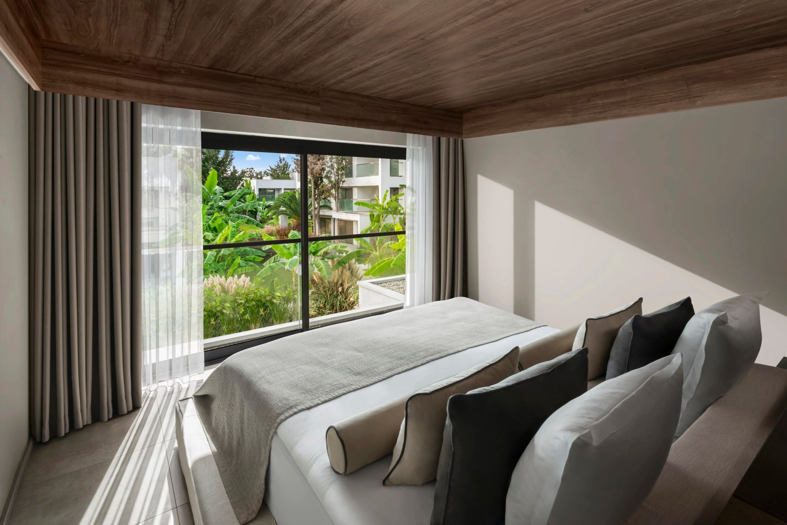 Helles Schlafzimmer mit Doppelbett, Holzdecke und großem Fenster zum Garten.