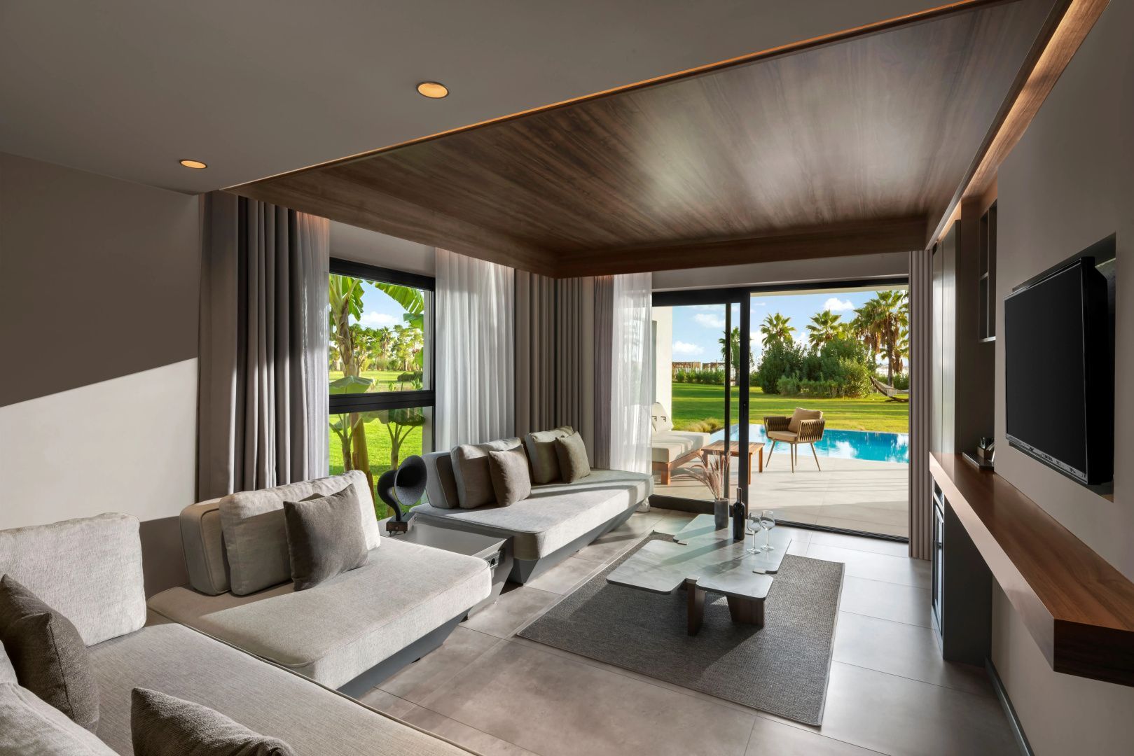 Sitzbereich einer Suite mit direktem Blick auf die Terrasse und einen angrenzenden Pool im Garten.