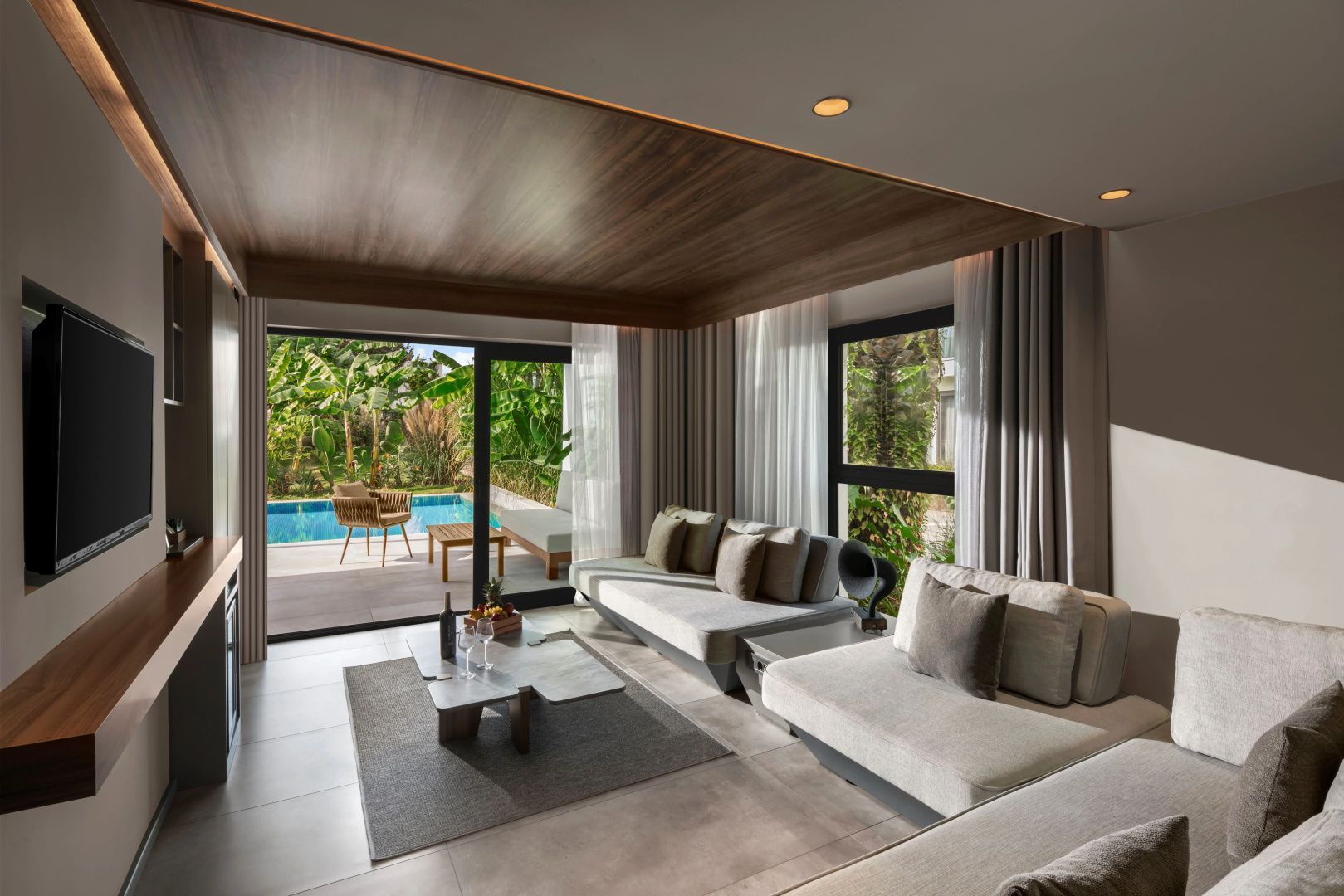 Geräumiger Wohnbereich einer Suite mit Sitzgelegenheiten und Fensterfront zum Poolbereich.