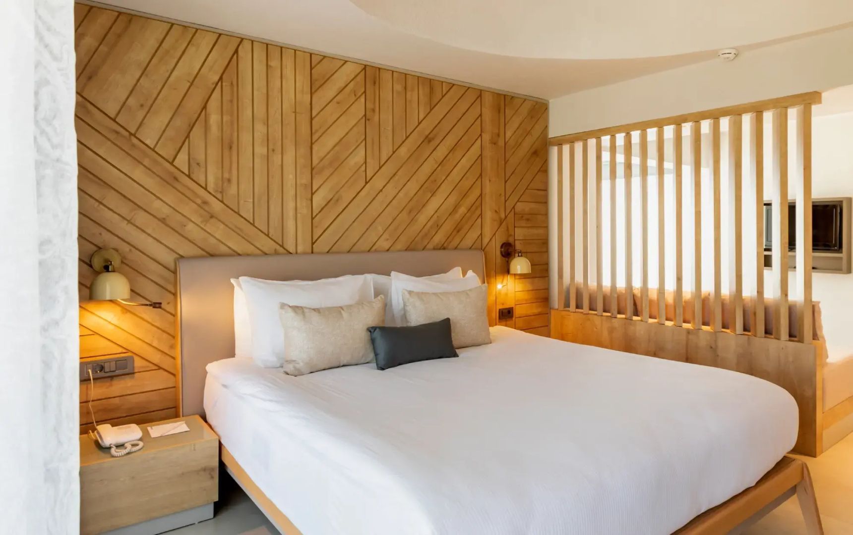 Doppelbett mit weißen Kissen vor einer dekorativen Holzwand im Hotelzimmer.