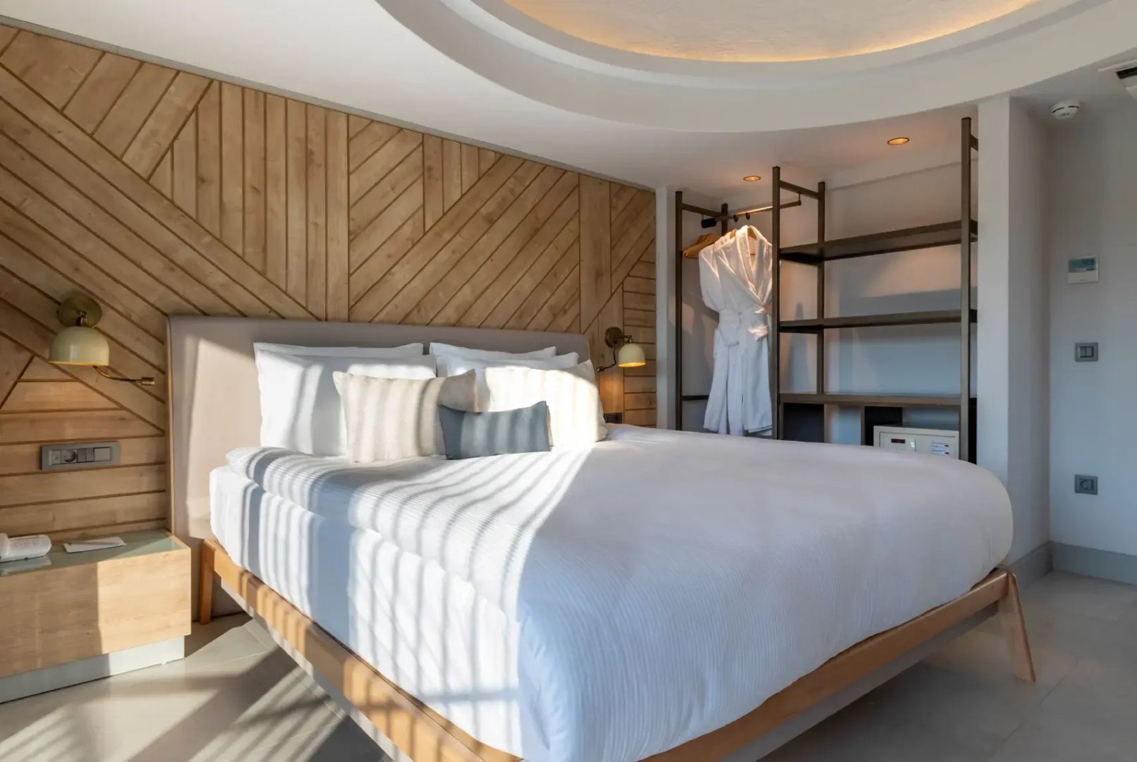 Doppelbett mit weißer Bettwäsche vor einer Wandverkleidung aus Holz im Hotelzimmer.