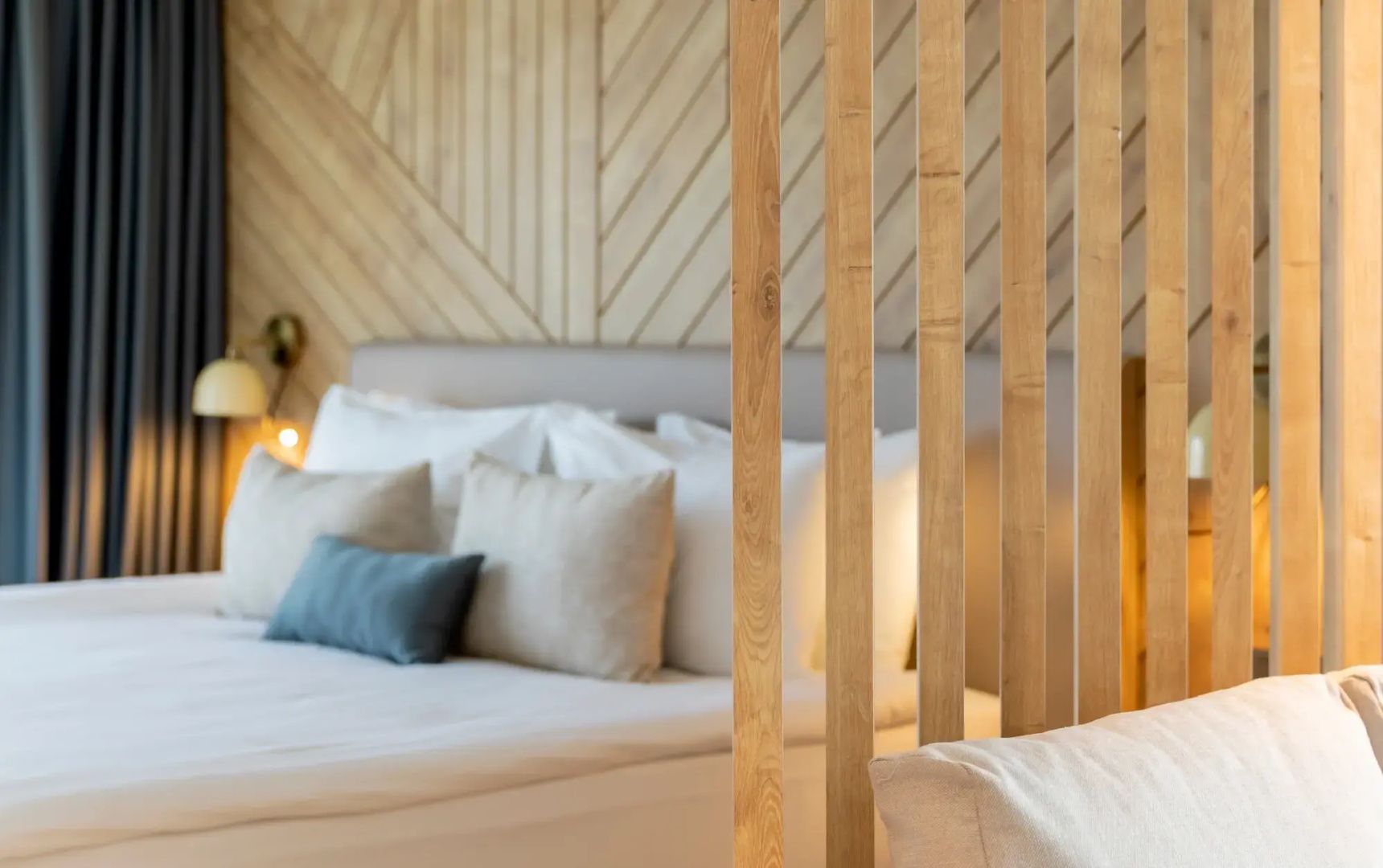 Blick durch ein Element aus Holzstreben auf ein gemachtes Bett im Zimmer.