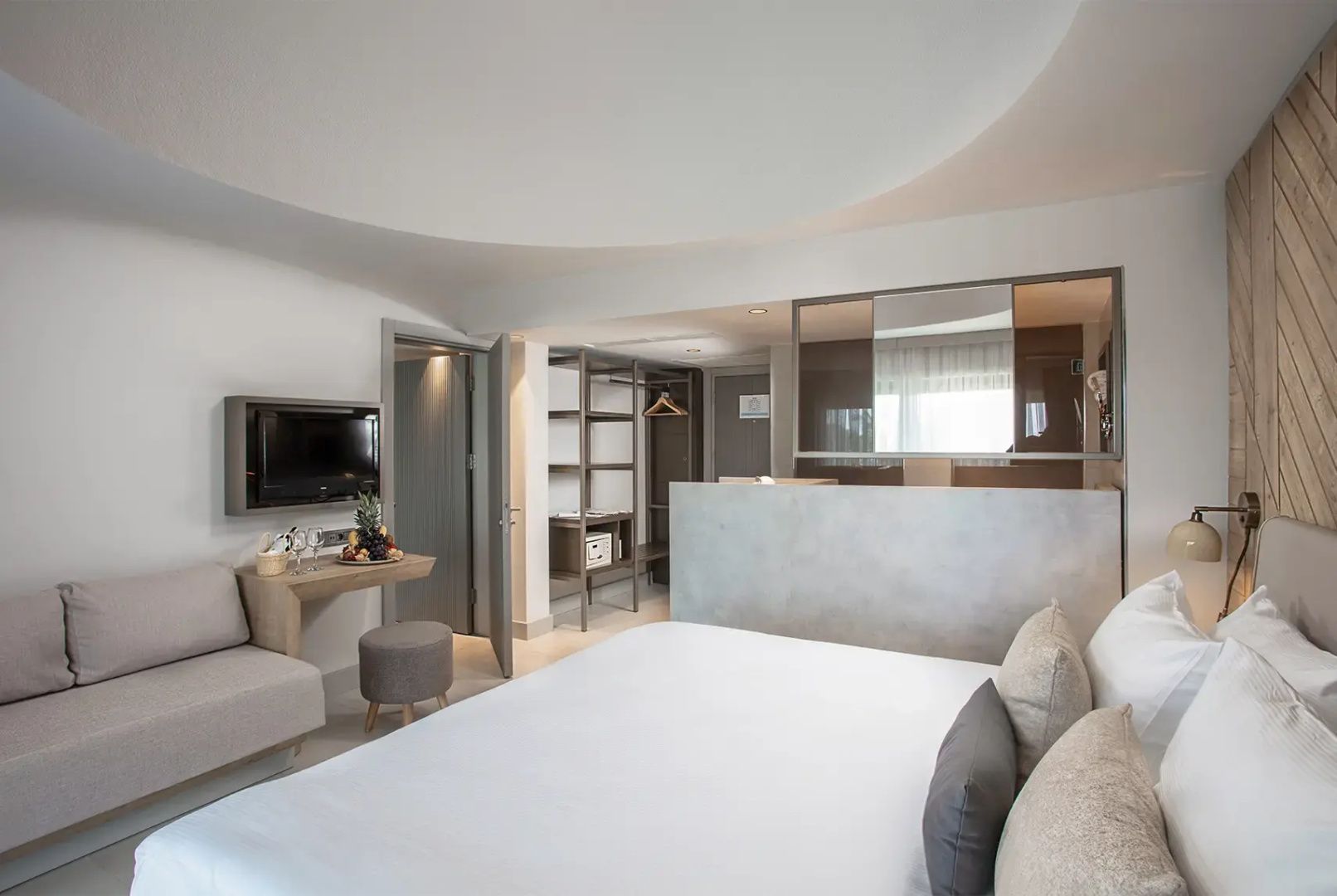Helles Hotelzimmer mit Doppelbett, Wandfernseher und integriertem Ankleidebereich.