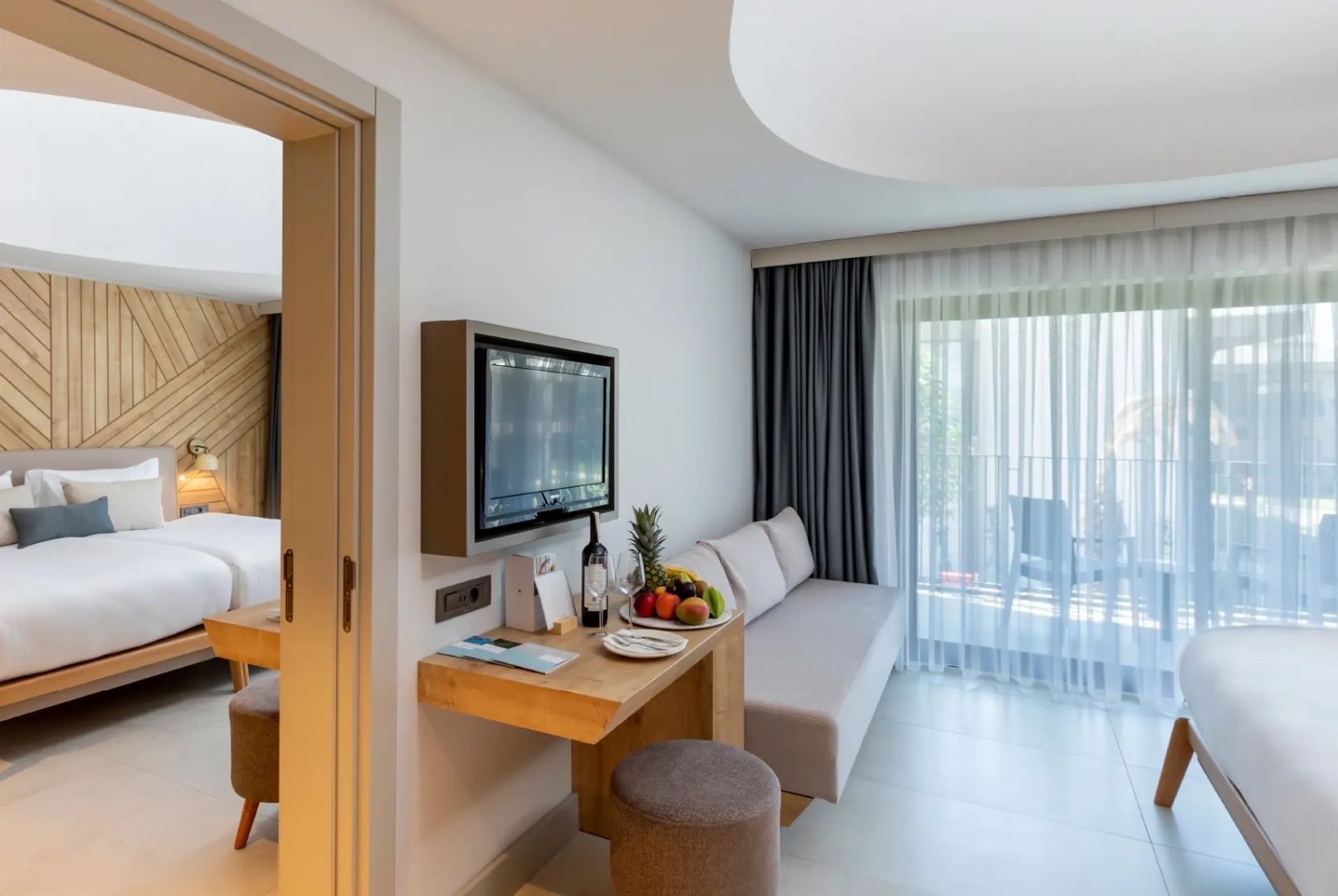 Wohnbereich eines Hotelzimmers mit Sofa, Schreibtisch und Zugang zum Balkon.