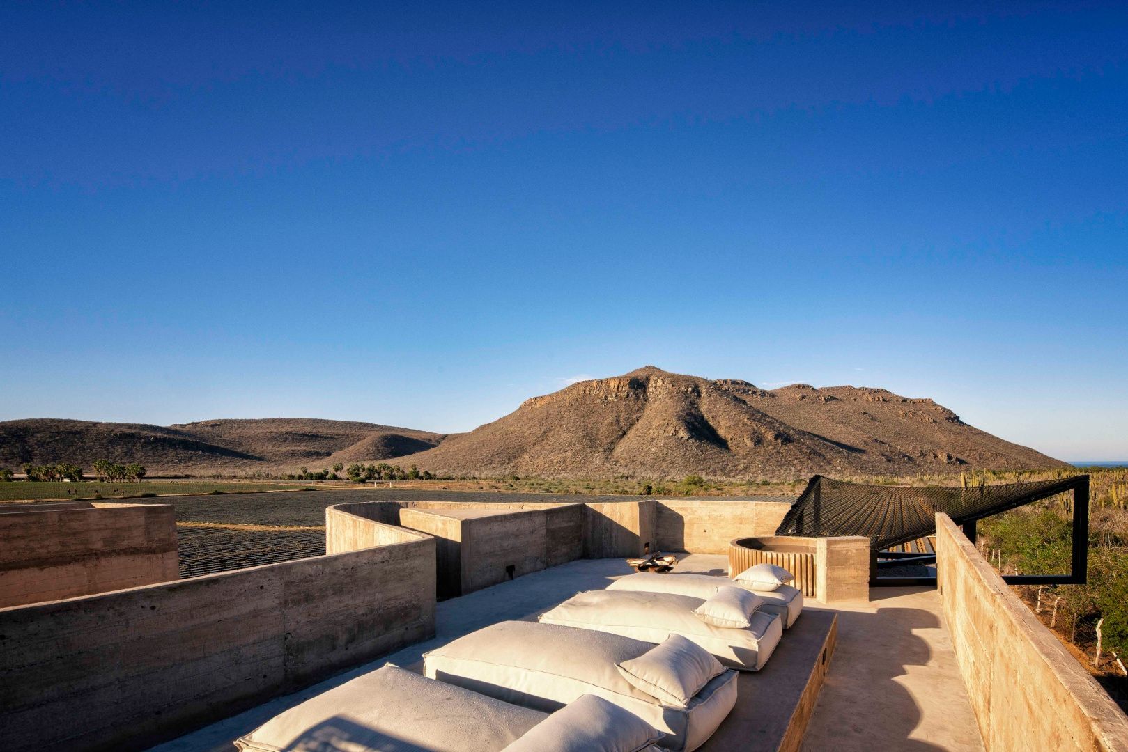 Dachterrasse mit Liegekissen und Blick auf eine trockene Berglandschaft unter blauem Himmel.