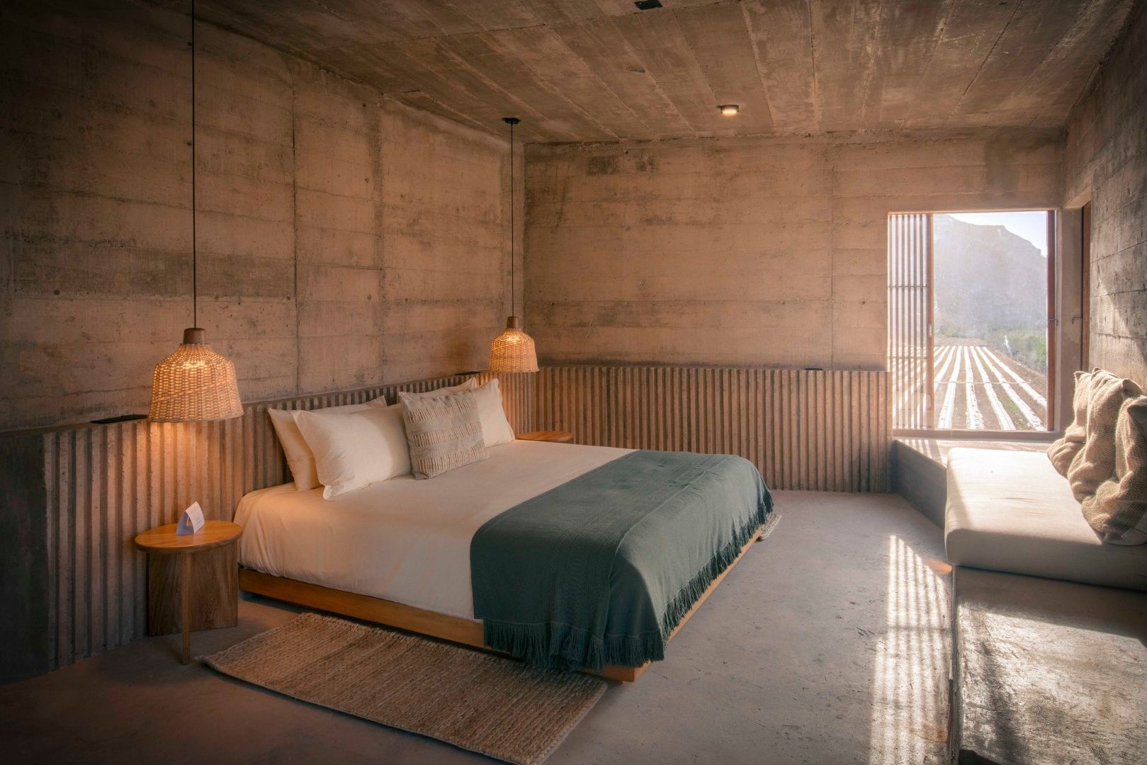 Doppelbett mit grüner Decke in einem hellen Zimmer aus Sichtbeton