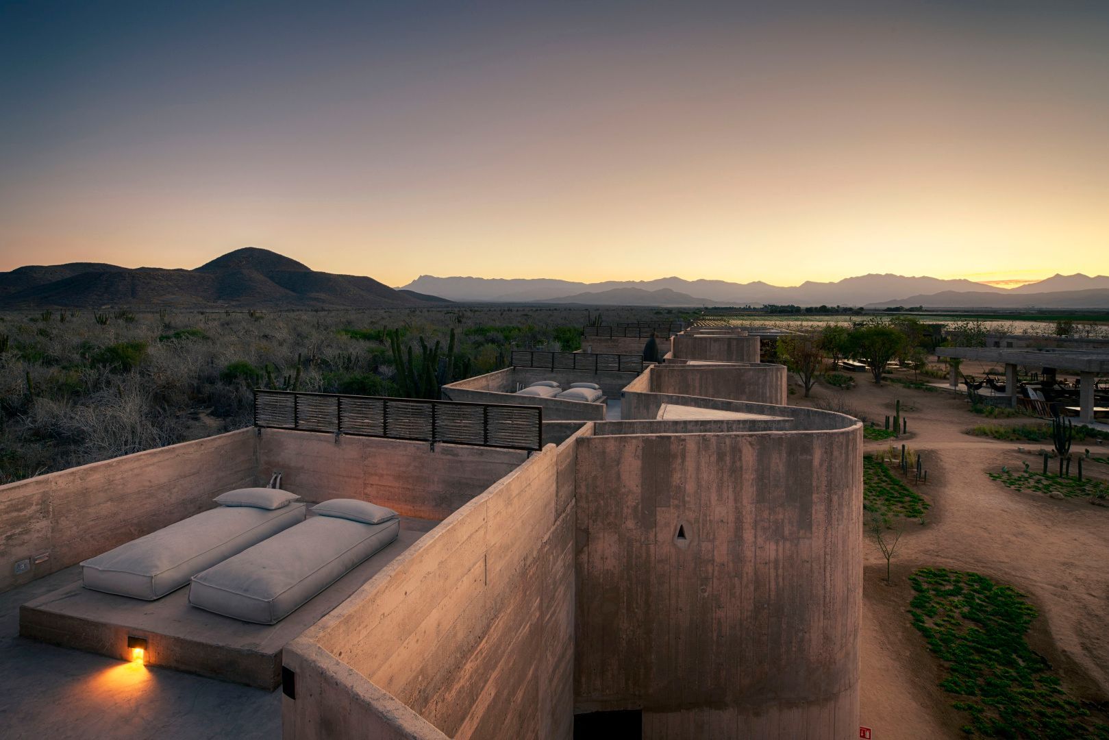 Dachterrasse aus Beton mit Liegekissen und Blick auf die Wüstenlandschaft und Berge.