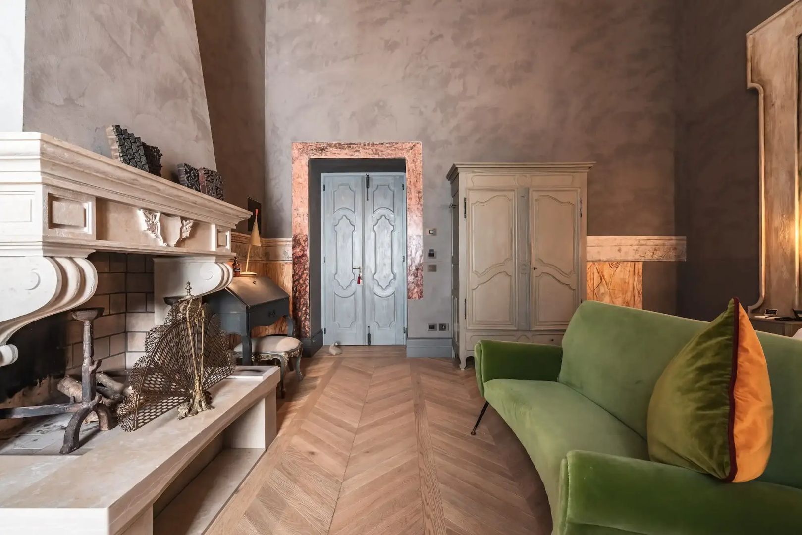 Wohnbereich mit grünem Sofa, Parkettboden im Fischgrätmuster und historischer Holztür.