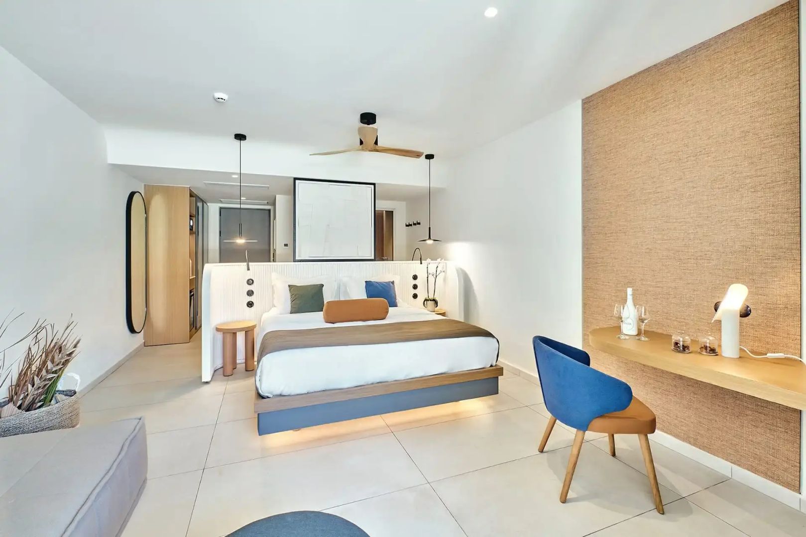 Hell gestaltetes Hotelzimmer mit großem Doppelbett, Deckenventilator und Schreibtisch.