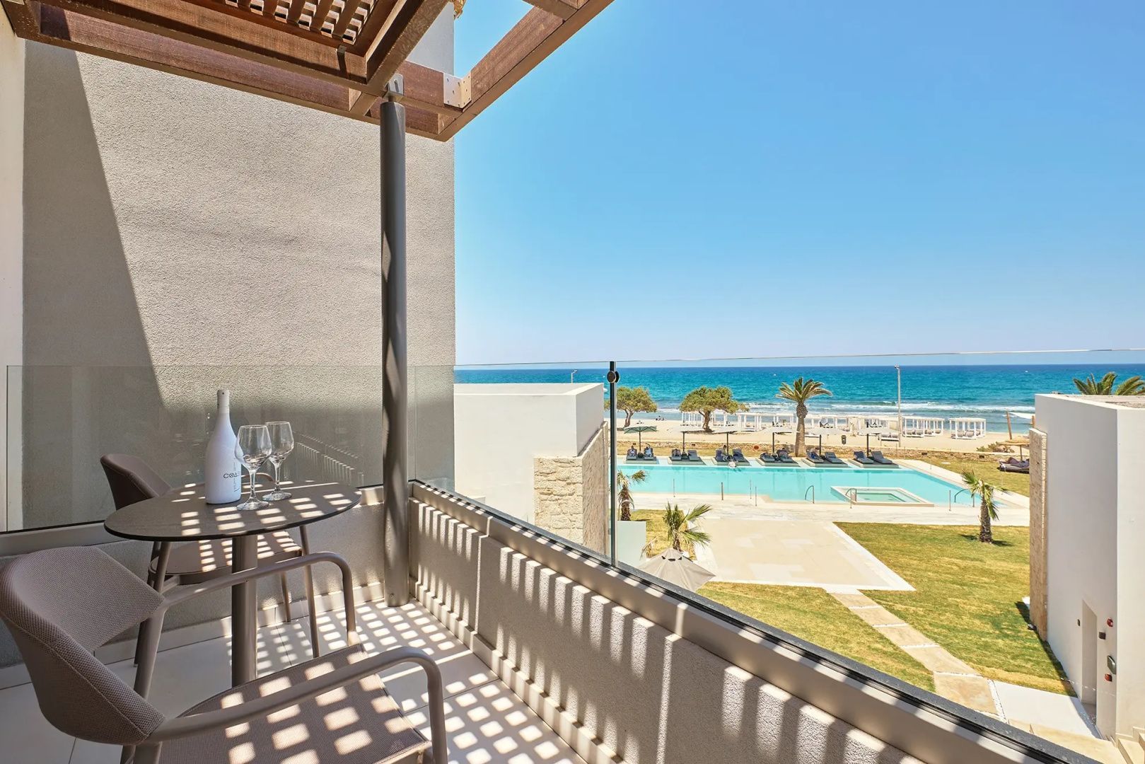 Aussicht vom Balkon mit Tisch und Stühlen auf eine gepflegte Poolanlage und das offene Meer.