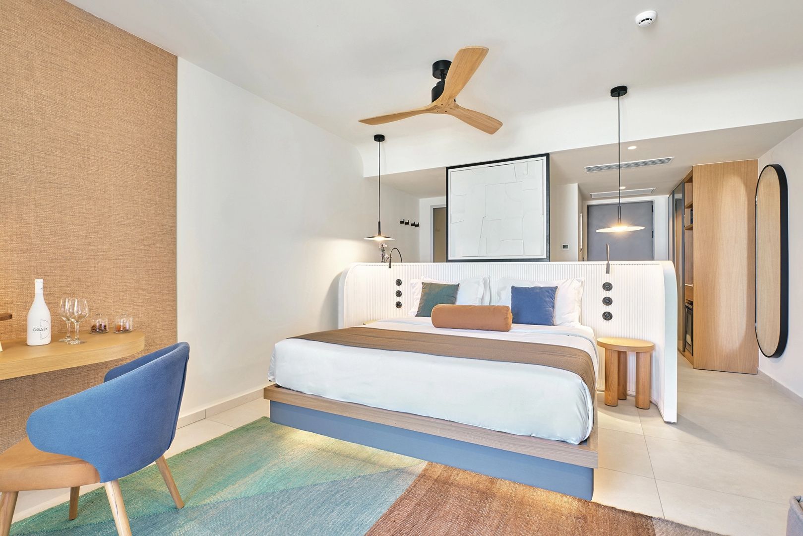 Doppelbett in hell gestaltetem Hotelzimmer mit Deckenventilator aus Holz und blauen Akzenten.