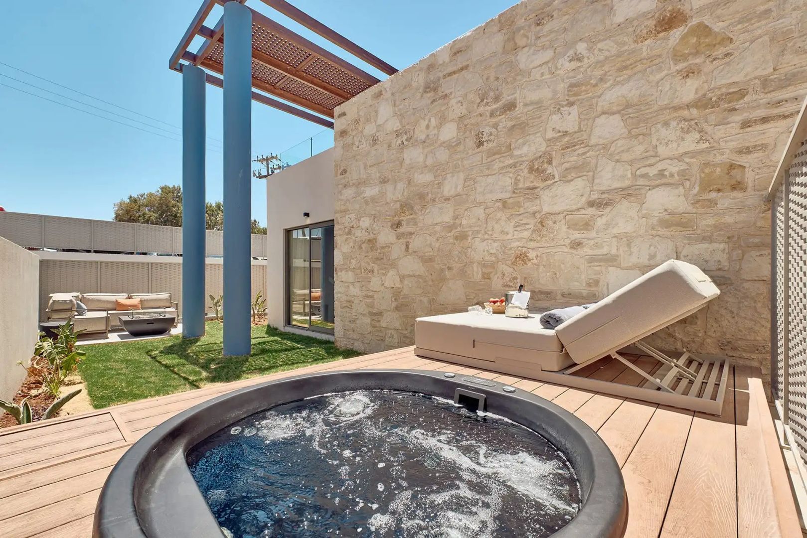 Eingebauter Whirlpool auf einer Holzterrasse neben einer Doppelliege und einer Steinmauer.