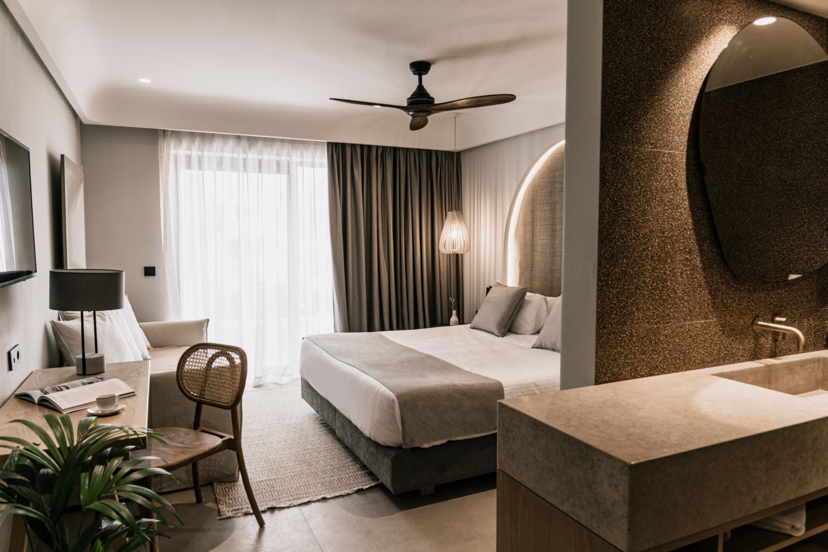 Hell eingerichtetes Hotelzimmer mit großem Doppelbett, Sessel und Balkontür.
