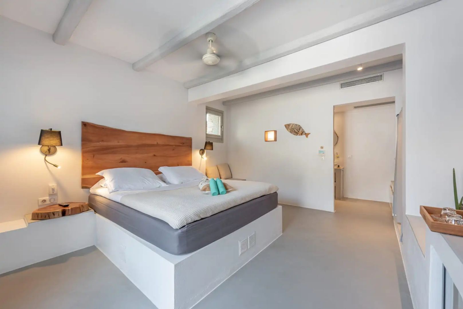 Helles Hotelzimmer mit Doppelbett, hölzernem Kopfteil und weiß gestrichenen Wänden.