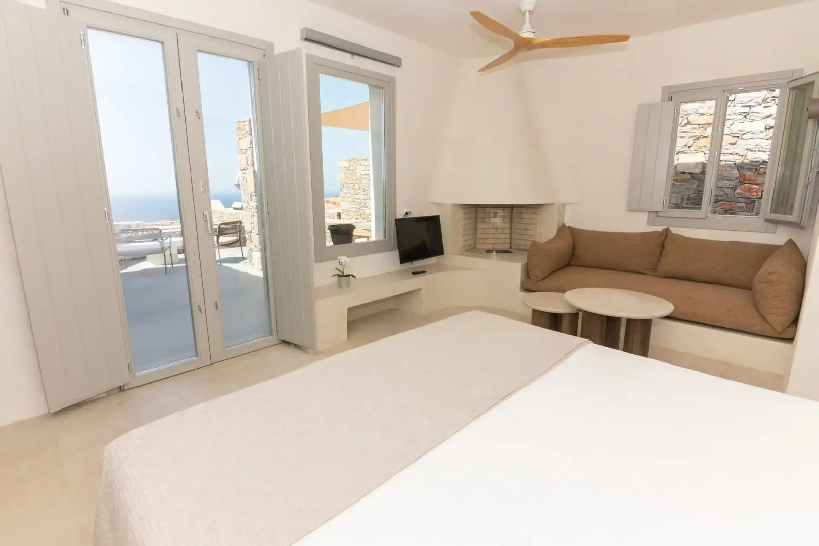 Helles Zimmer mit weißem Bett, Kamin in der Ecke, Sofa und Meerblick durch die Balkontür.