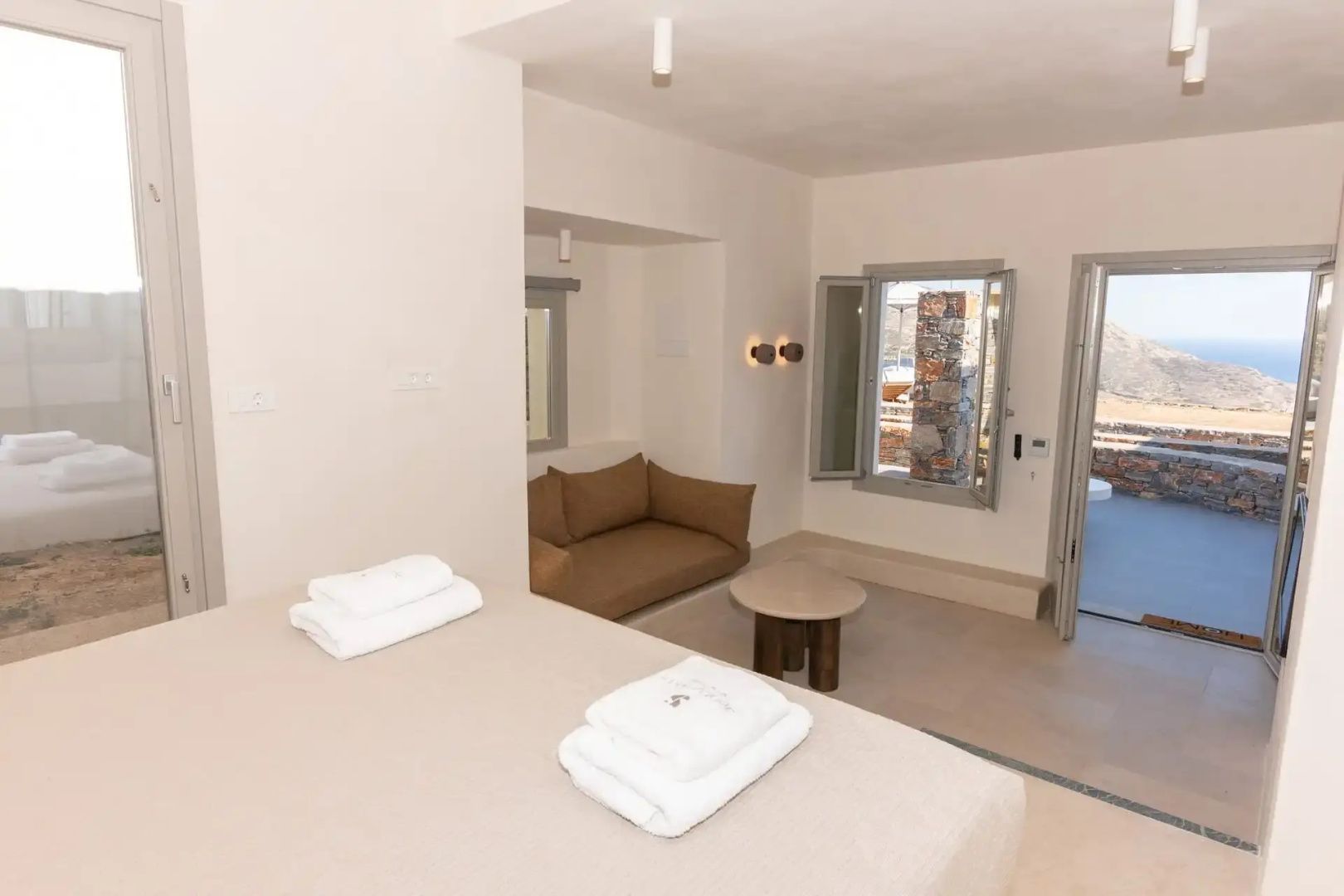 Blick vom Bett mit Handtüchern auf eine braune Sitzecke mit Sofa und Beistelltisch.