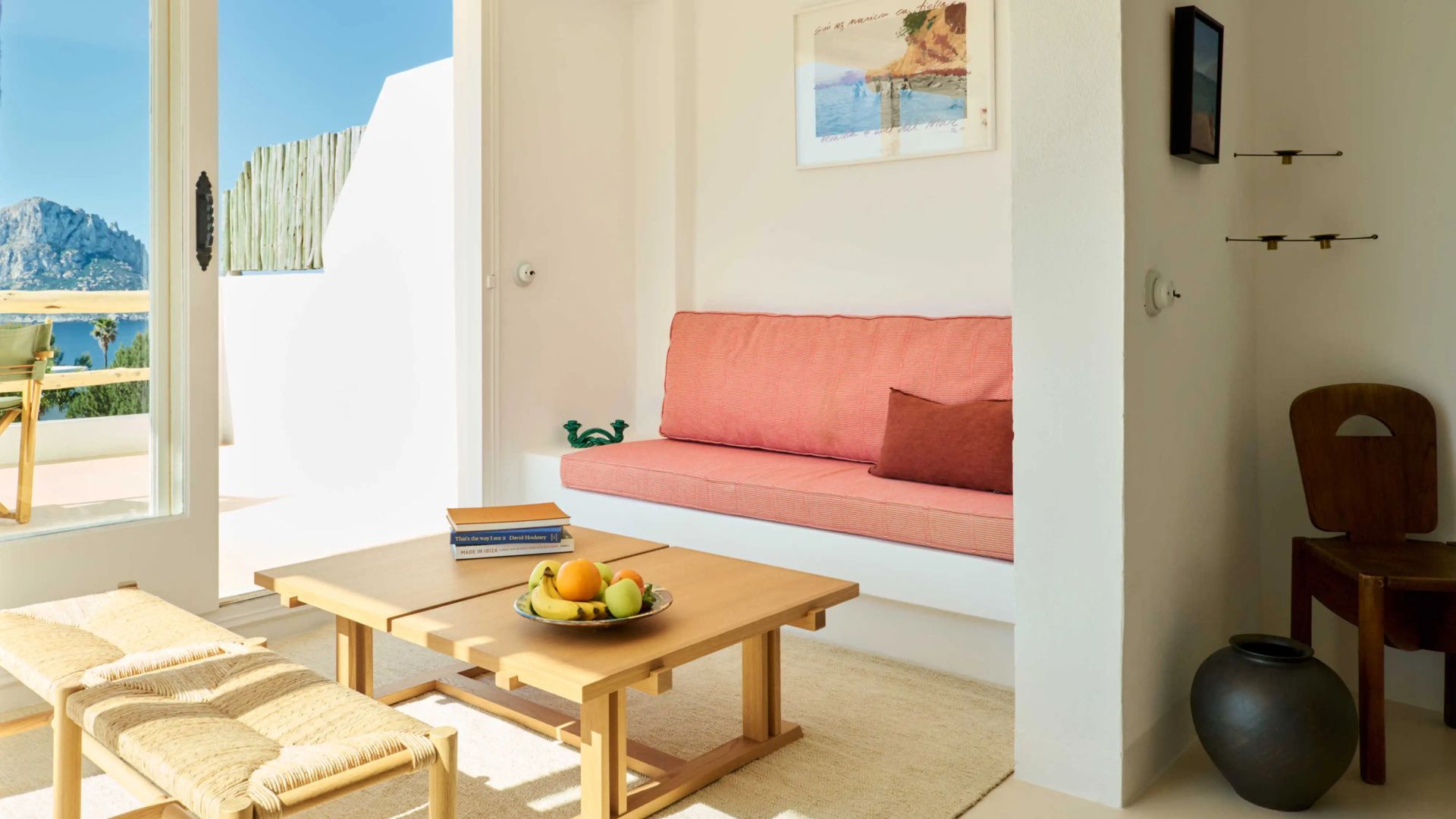 Sitzecke im Zimmer mit rosa Polsterbank, Holztisch und einer Schale mit frischem Obst.
