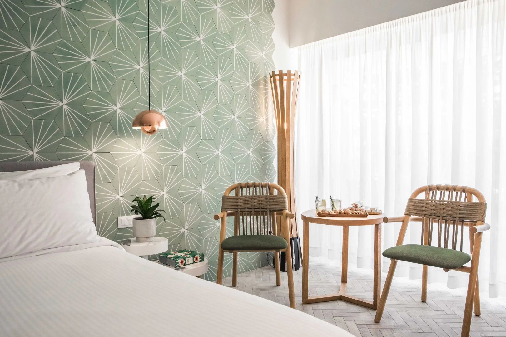 Sitzbereich im Hotelzimmer mit grüner Motivtapete, Holzstühlen und kleiner Tischgruppe.
