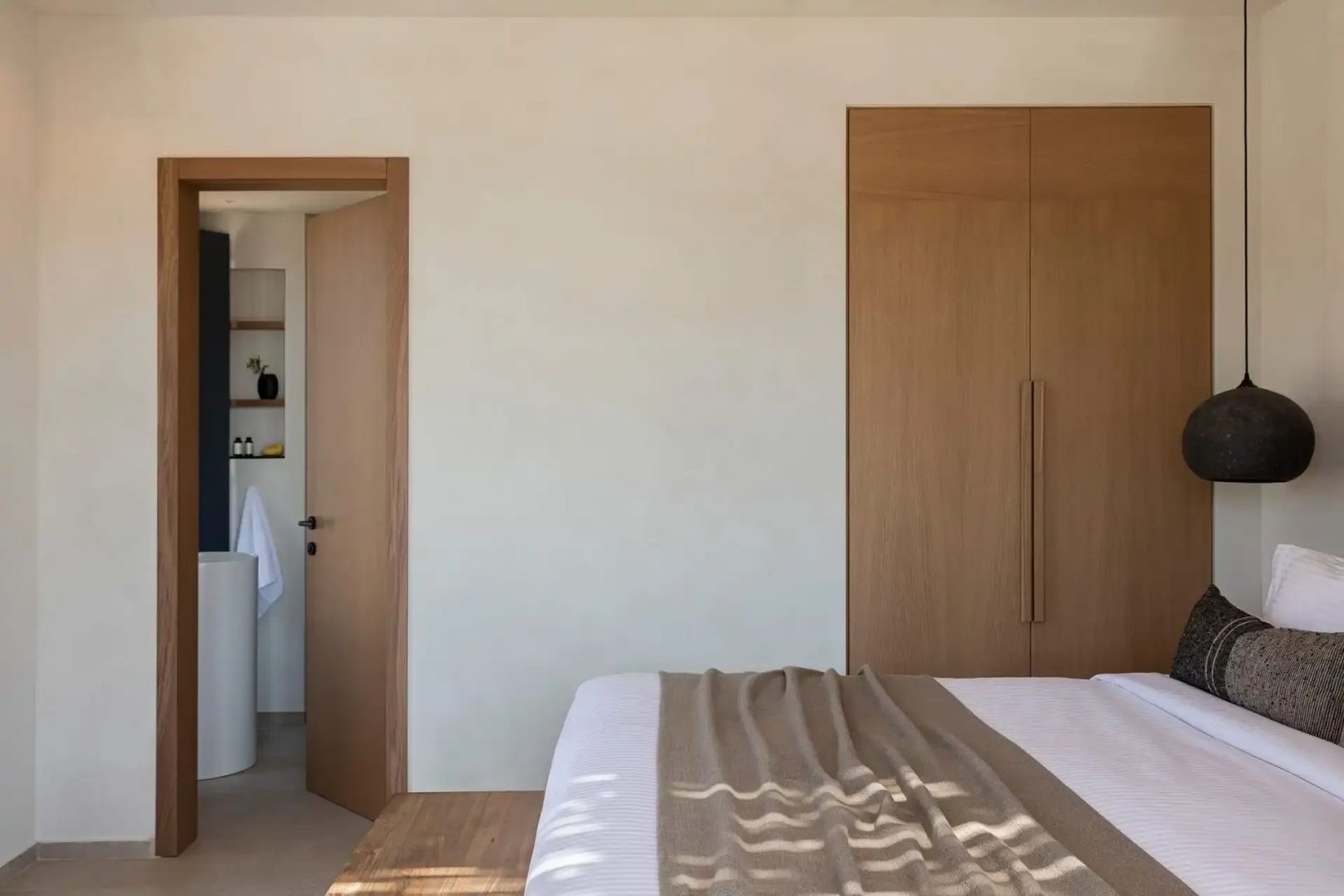 Schlafzimmer mit Holzschrank, hellem Bett und Durchgang zum Bad.