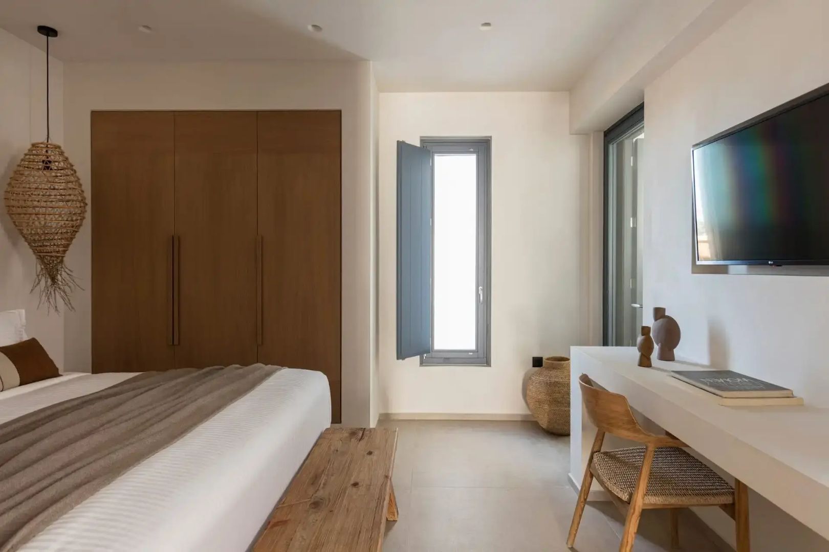 Hell eingerichtetes Hotelzimmer mit Holzschrank, Schreibtisch und Holzbank vor dem Bett.