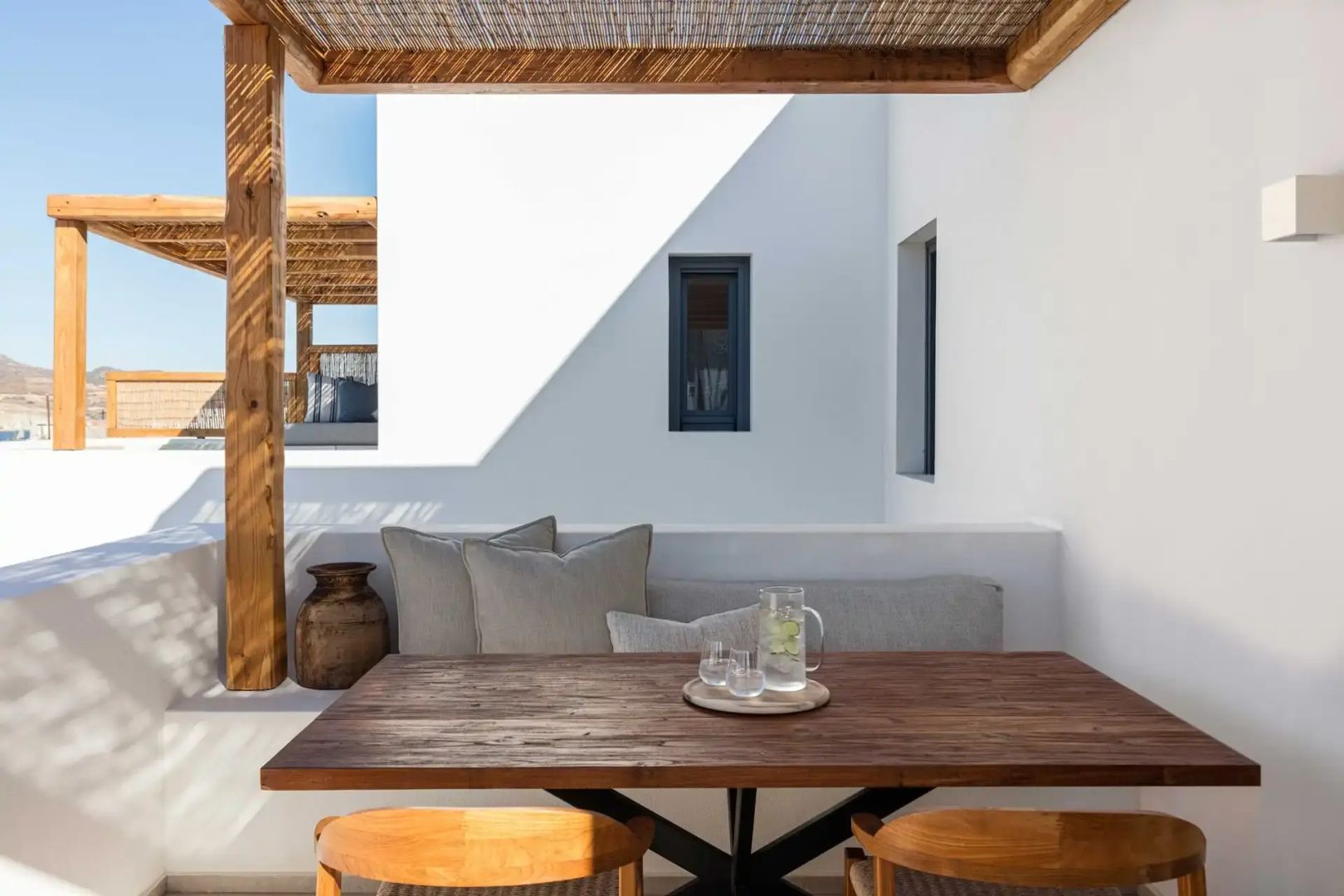 Überdachte Terrasse mit Holzesstisch, passenden Stühlen und Kissen auf der gemauerten Sitzbank.