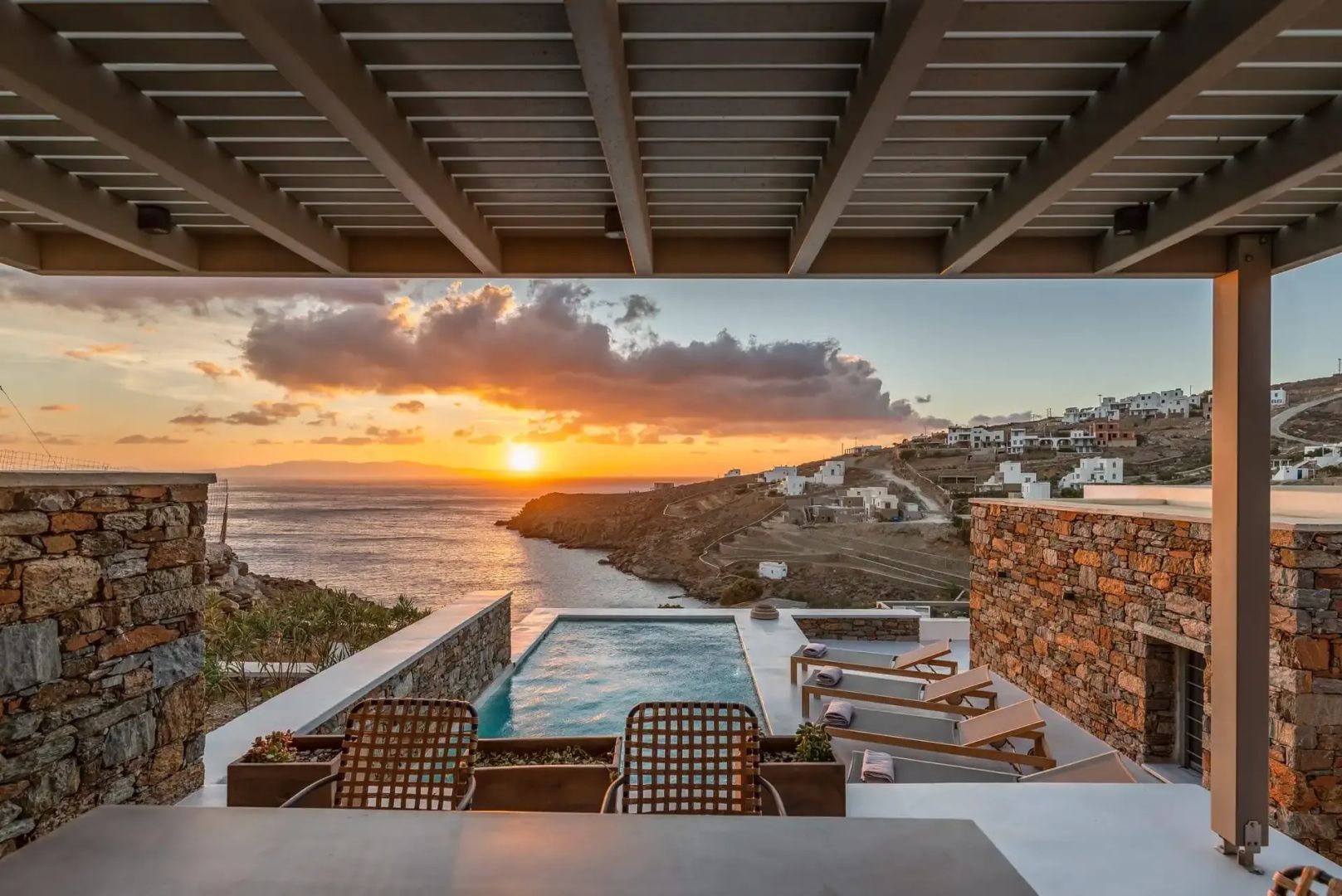 Überdachte Terrasse mit Swimmingpool und Sonnenliegen bei Sonnenuntergang über dem Meer.