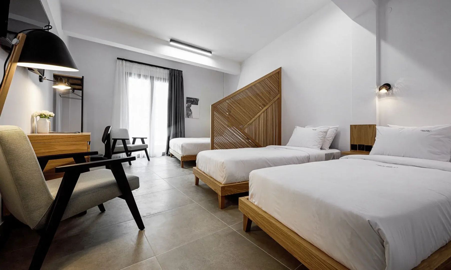Helles Hotelzimmer mit mehreren Einzelbetten, Holztrennwand und Balkontür.
