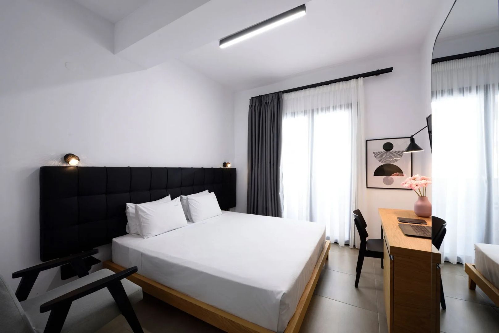 Modernes Hotelzimmer mit großem Doppelbett, schwarzem Kopfteil und Schreibtisch am Fenster.