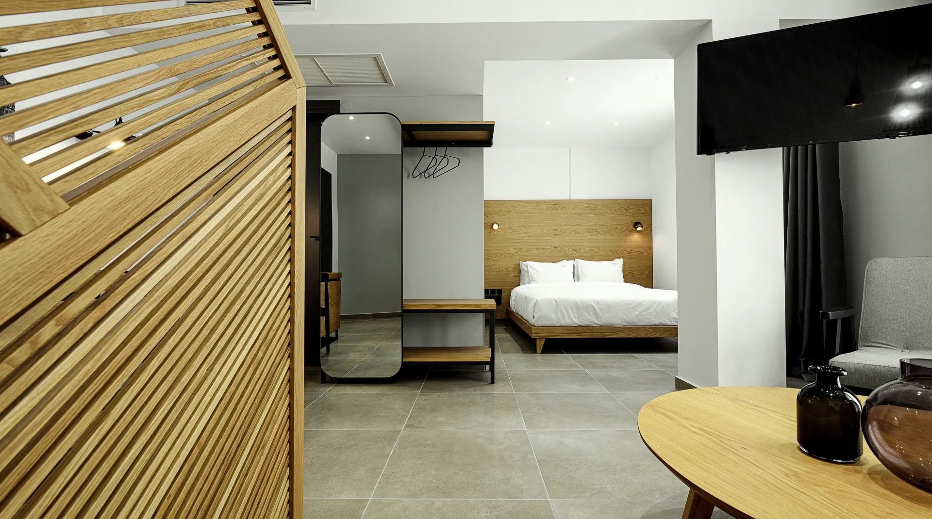 Modernes Hotelzimmer mit Doppelbett, Ganzkörperspiegel und Raumteiler aus Holz.