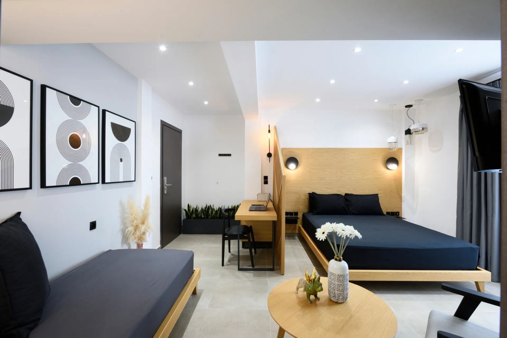 Doppelbett mit schwarzer Bettwäsche, Schreibtisch und Sitzbereich in modern eingerichtetem Zimmer.