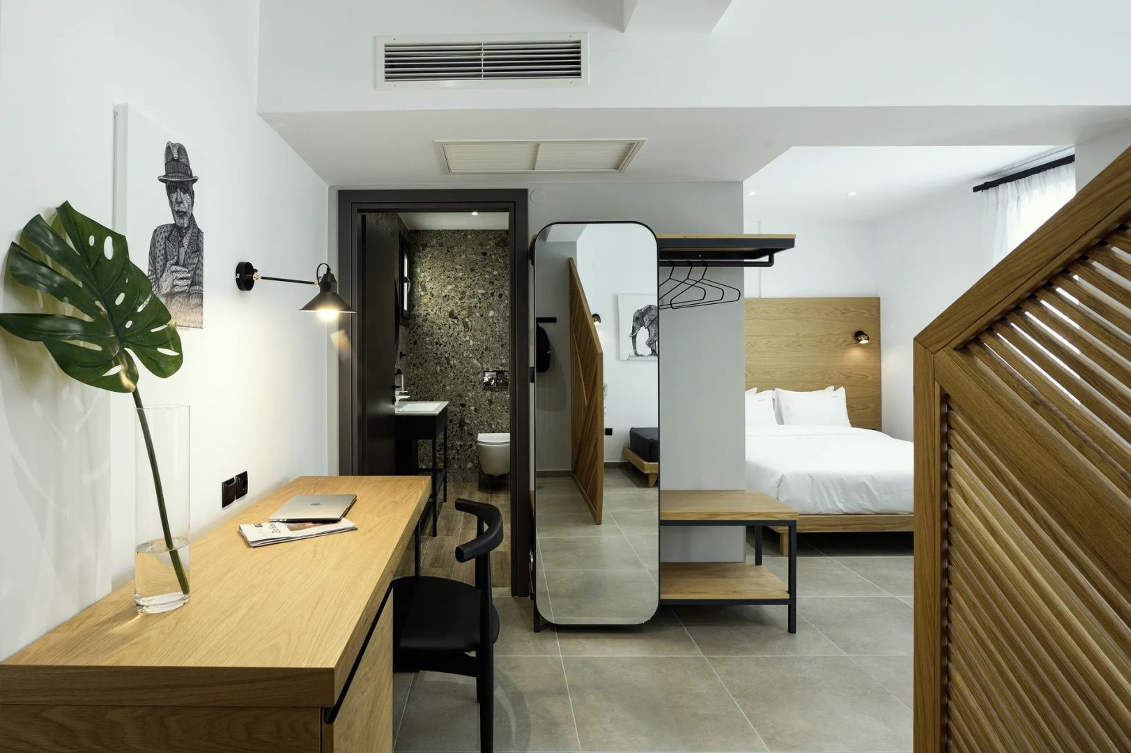 Zimmer mit Holzschreibtisch, Stuhl, Spiegel sowie Zugang zum Badezimmer.