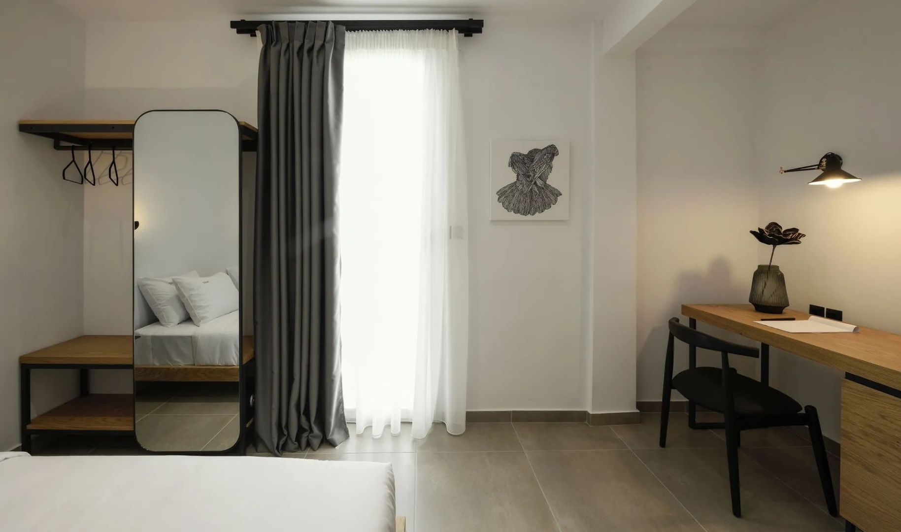 Helles Hotelzimmer mit bodentiefem Fenster, grauen Vorhängen und Ankleidespiegel.