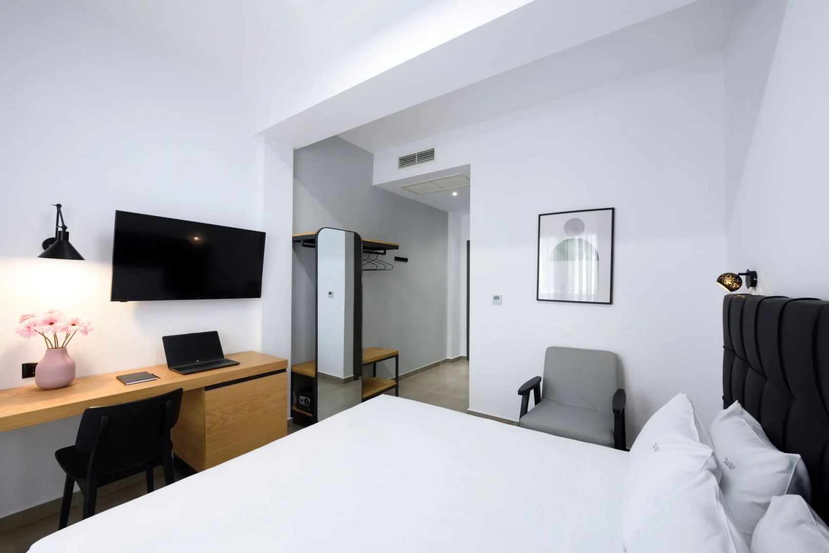 Blick im Hotelzimmer vom Bett aus auf Sessel, Wandfernseher und den offenen Flurbereich.