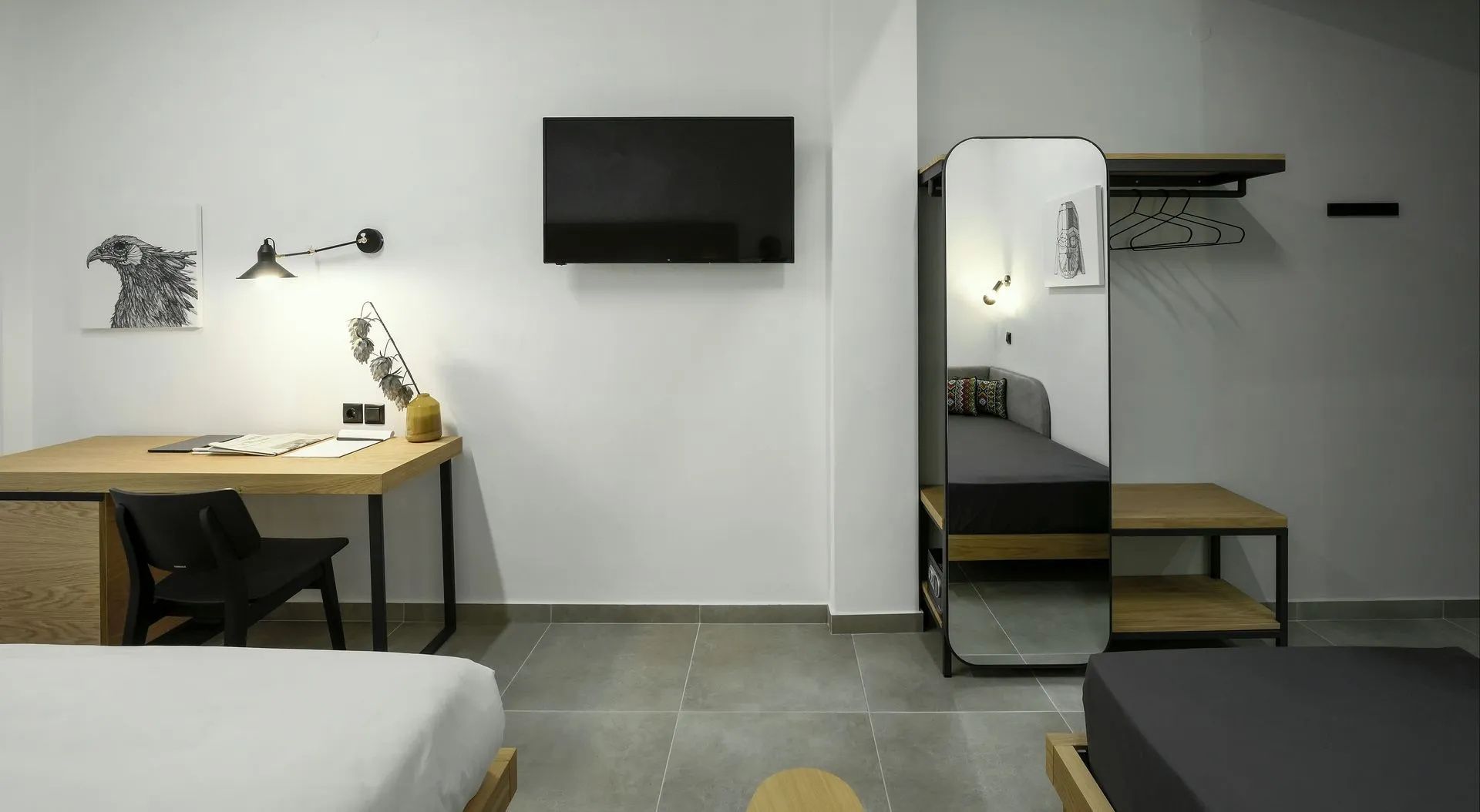 Wandausschnitt mit Flachbildfernseher, hohem Standspiegel und Schreibtischbereich im Zimmer.