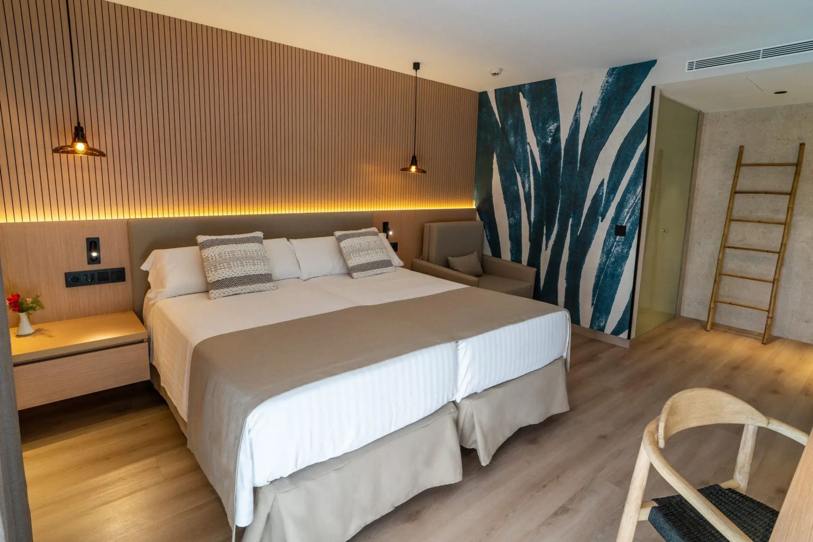 Doppelbett mit hellbrauner Tagesdecke, Holzvertäfelung an der Wand und blauem Muster an der Seite.