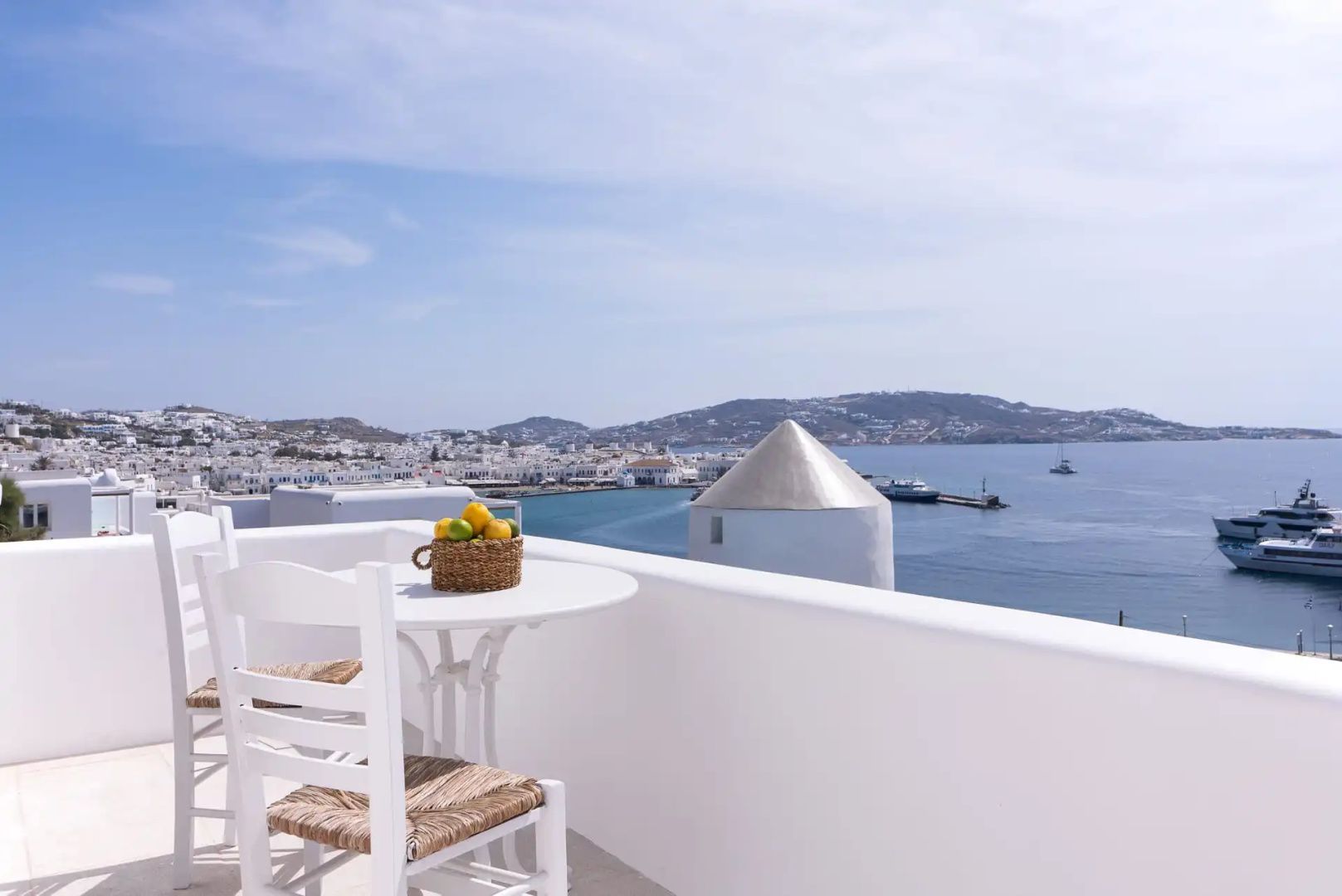 Balkon mit weißem Tisch und Stühlen sowie Blick auf das Meer und die Stadt Mykonos.