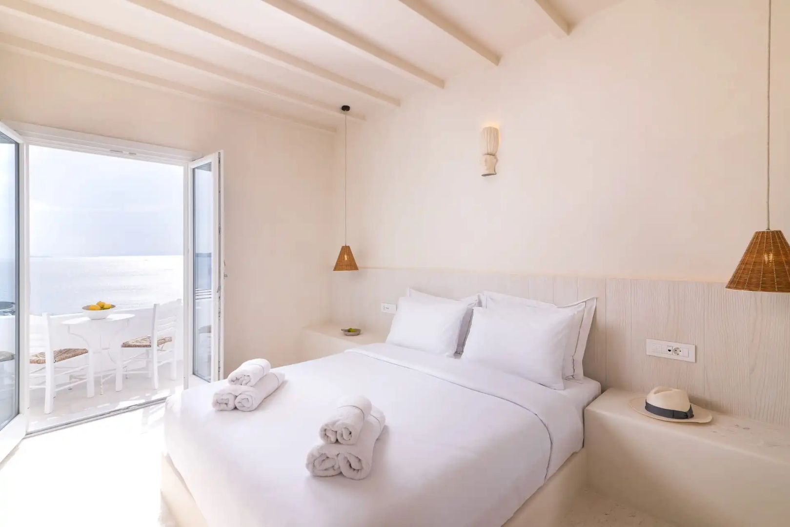 Schlafzimmer in hellen Tönen mit großem Doppelbett, Balkonzugang und Holzdecke.