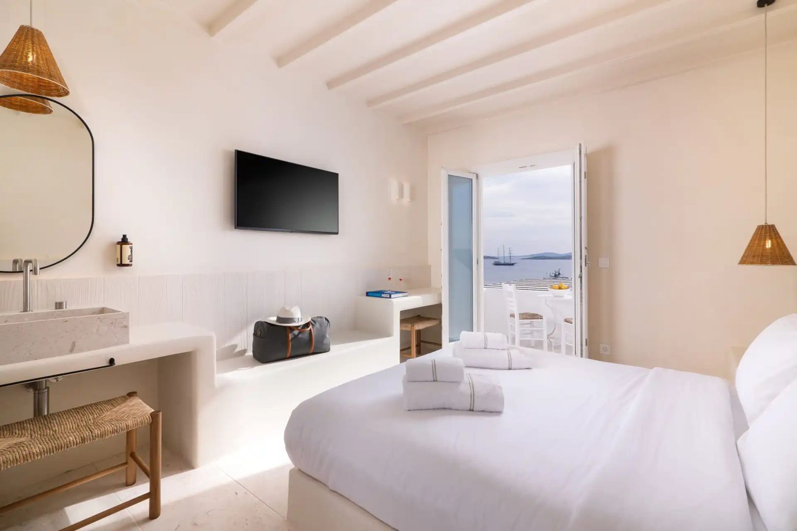 Helles Hotelzimmer mit Doppelbett, Wand-TV und Balkontür mit Blick auf das Meer.